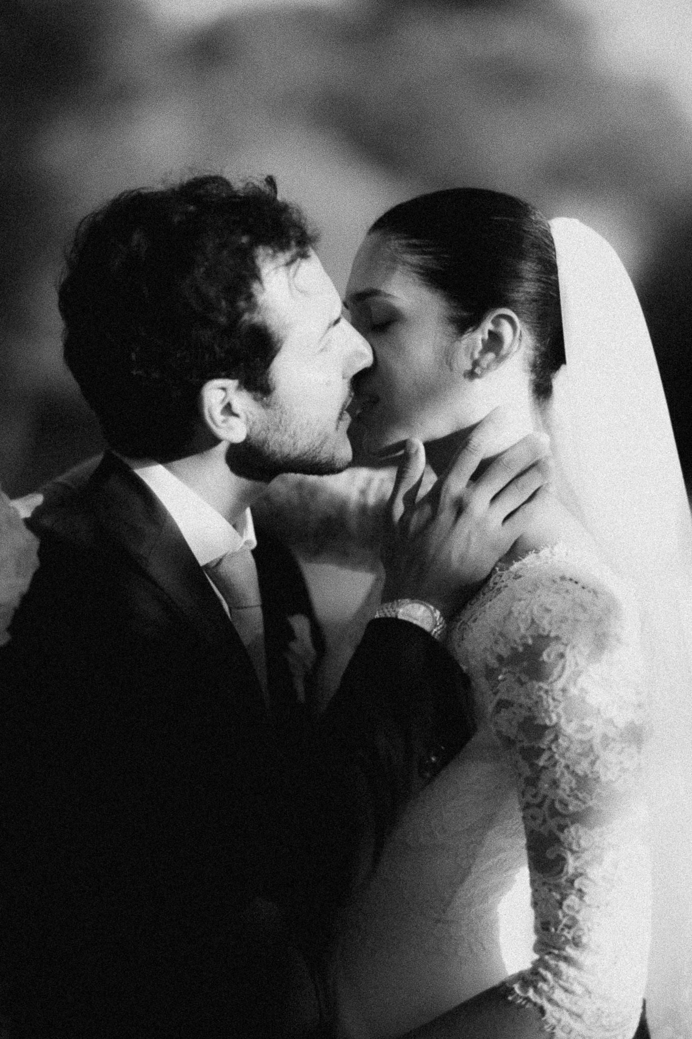 Black and white wedding photo of groom tenderly holding brides face for a kiss, both in elegant attire.