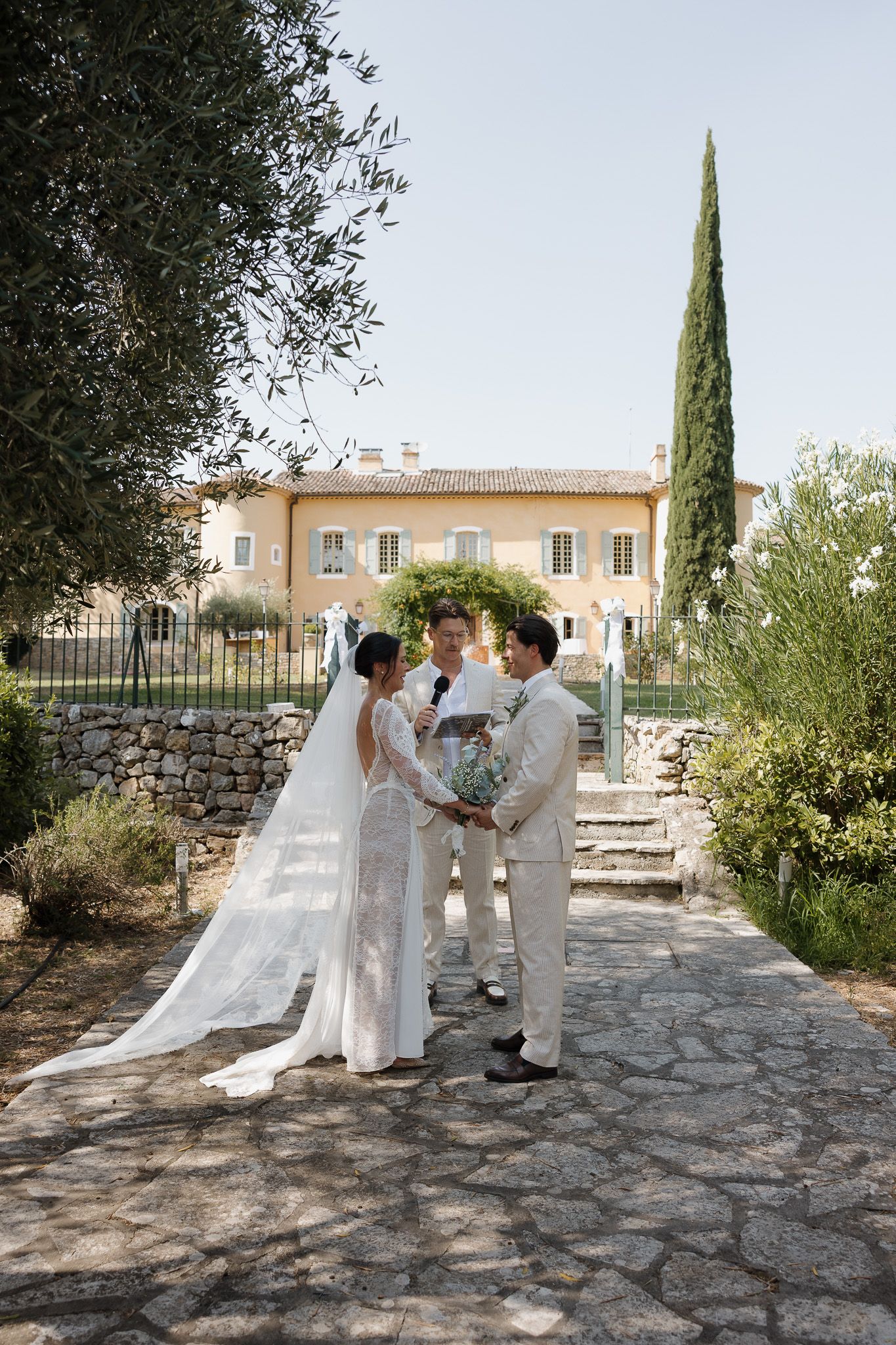 Bride and groom exchange vows with officiant at outdoor wedding ceremony at a Provençal villa in France.