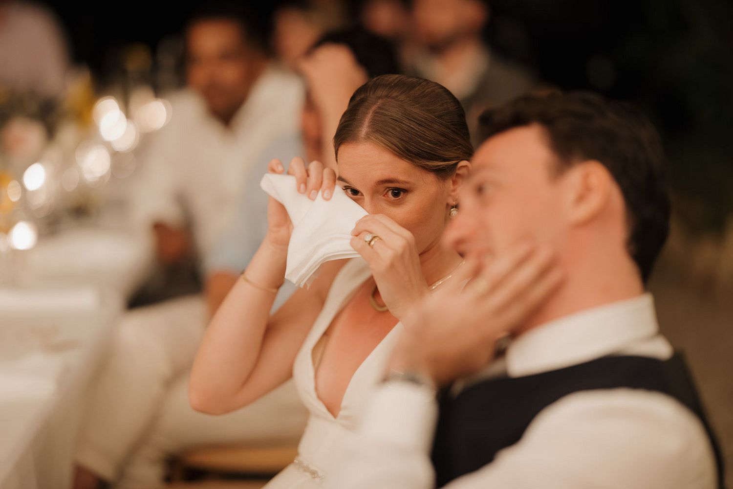 Wedding guests wipe away tears during an emotional moment at an indoor reception ceremony.