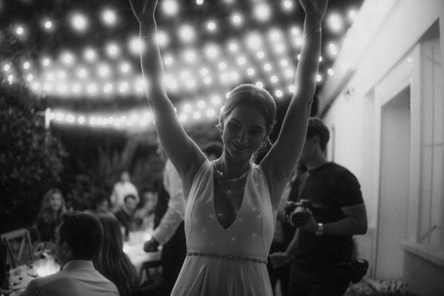 A string of glowing lights illuminates a romantic outdoor wedding reception with dancing silhouettes at dusk.