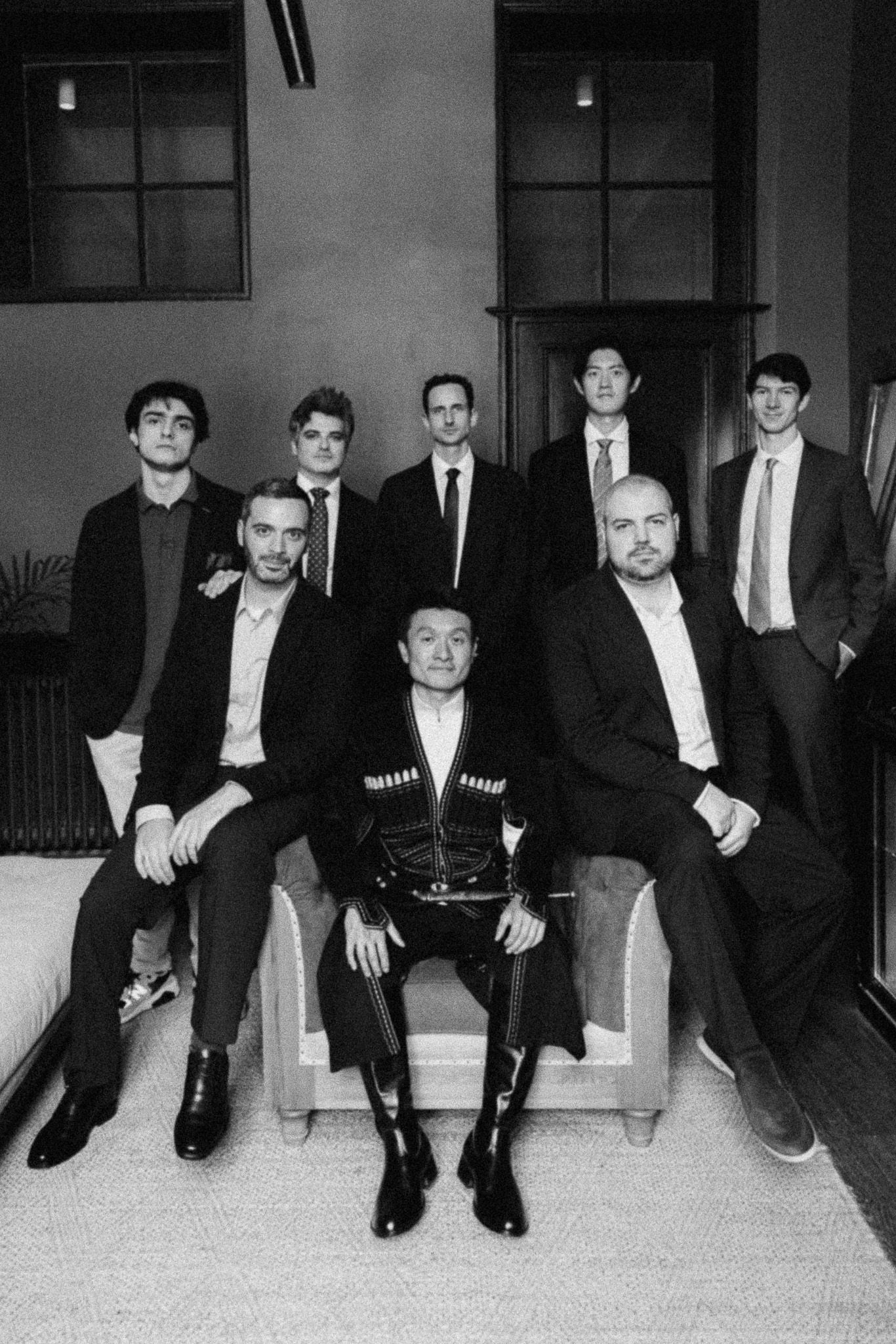 Black and white group photo of eight men in formal suits posing together indoors.