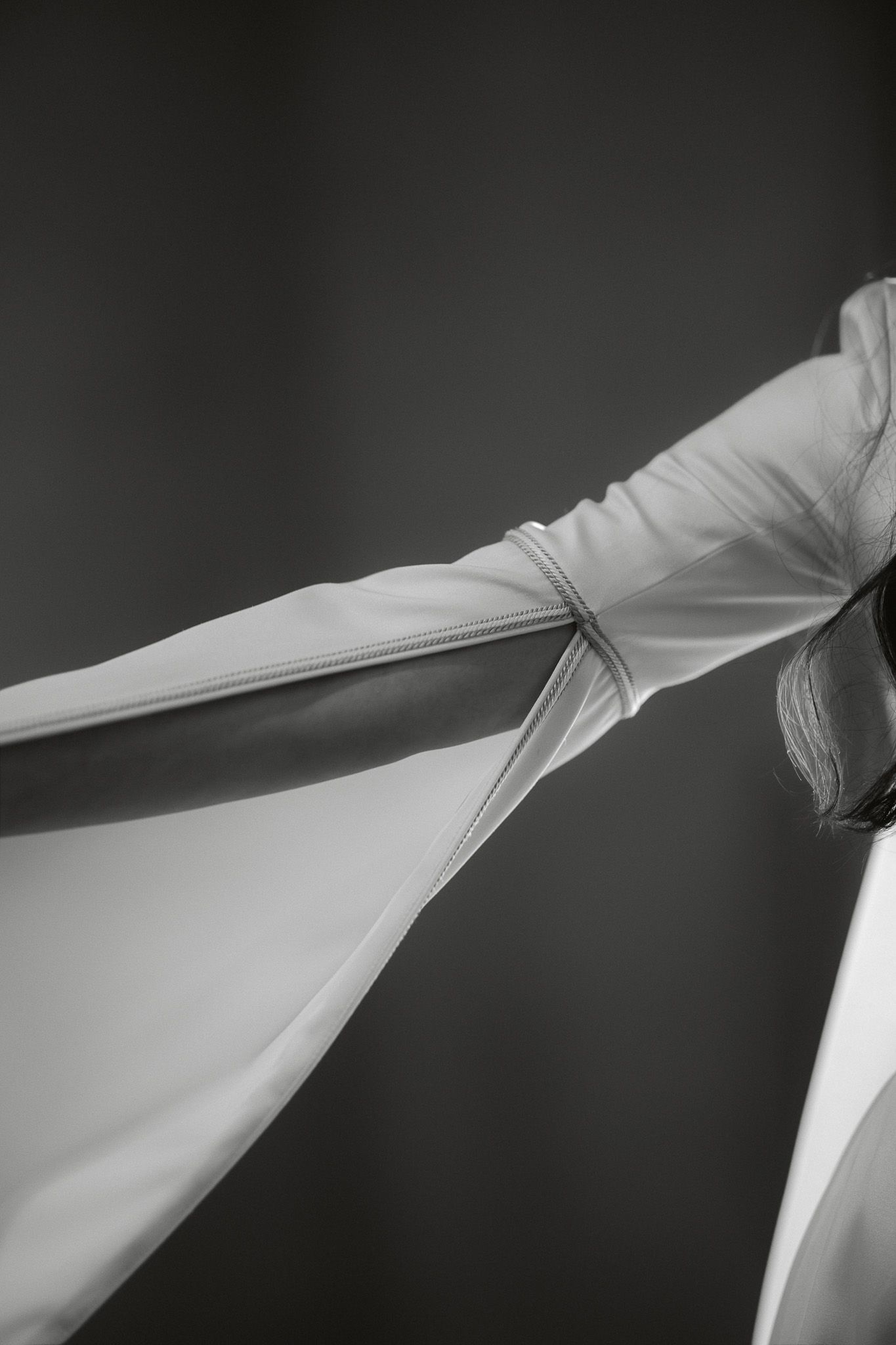 Black and white photo of a person in flowing white fabric, arms outstretched gracefully against a dark background.