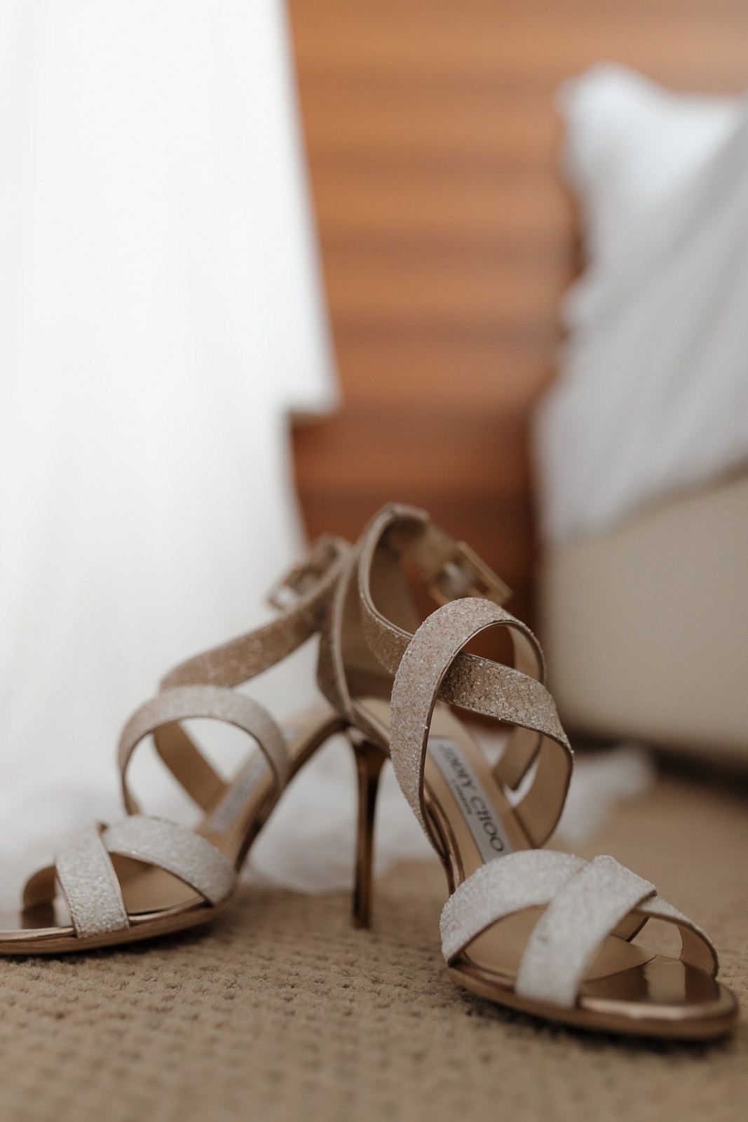 Beige strappy sandals with sparkly details arranged on a textured carpet.