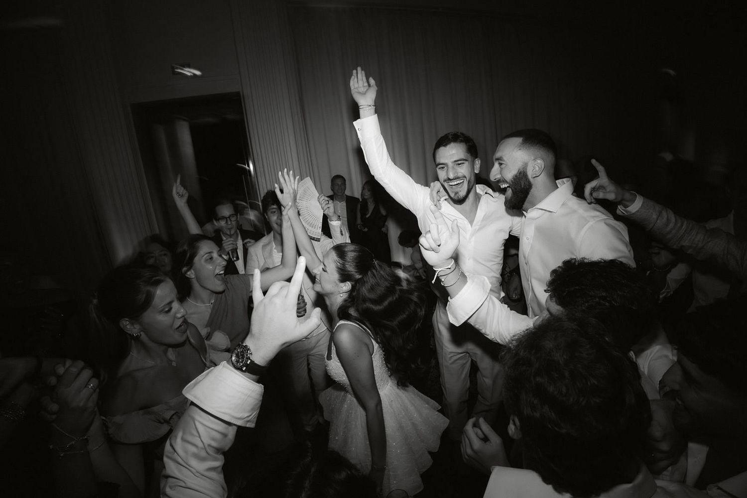 People dancing and celebrating at a lively party with hands raised in a dark venue.