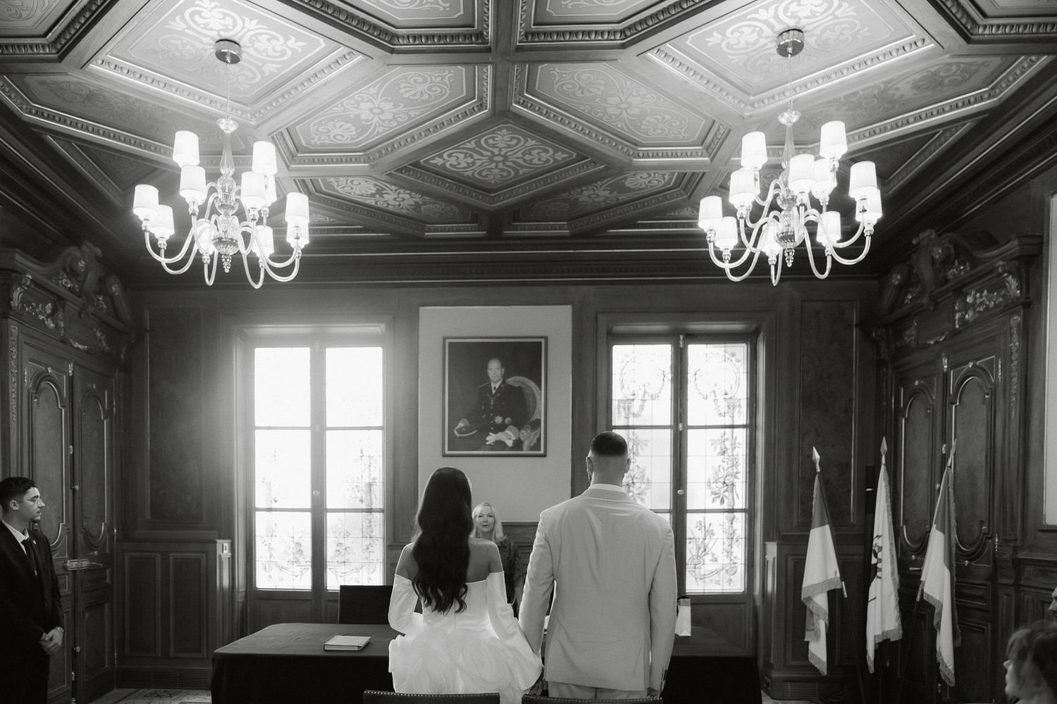 Elegant black and white interior of a historic mansion with ornate chandeliers and wood-paneled walls illuminated by natural light.