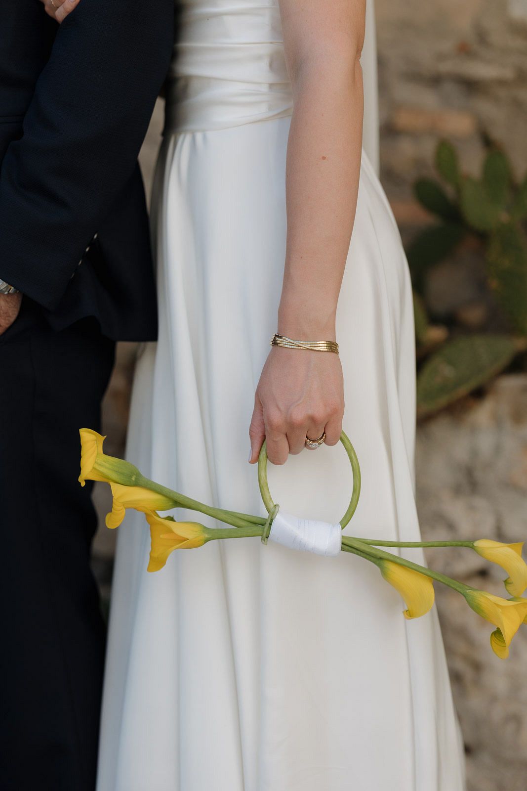 Close-up view of yellow calla lilies held against a white wedding dress.