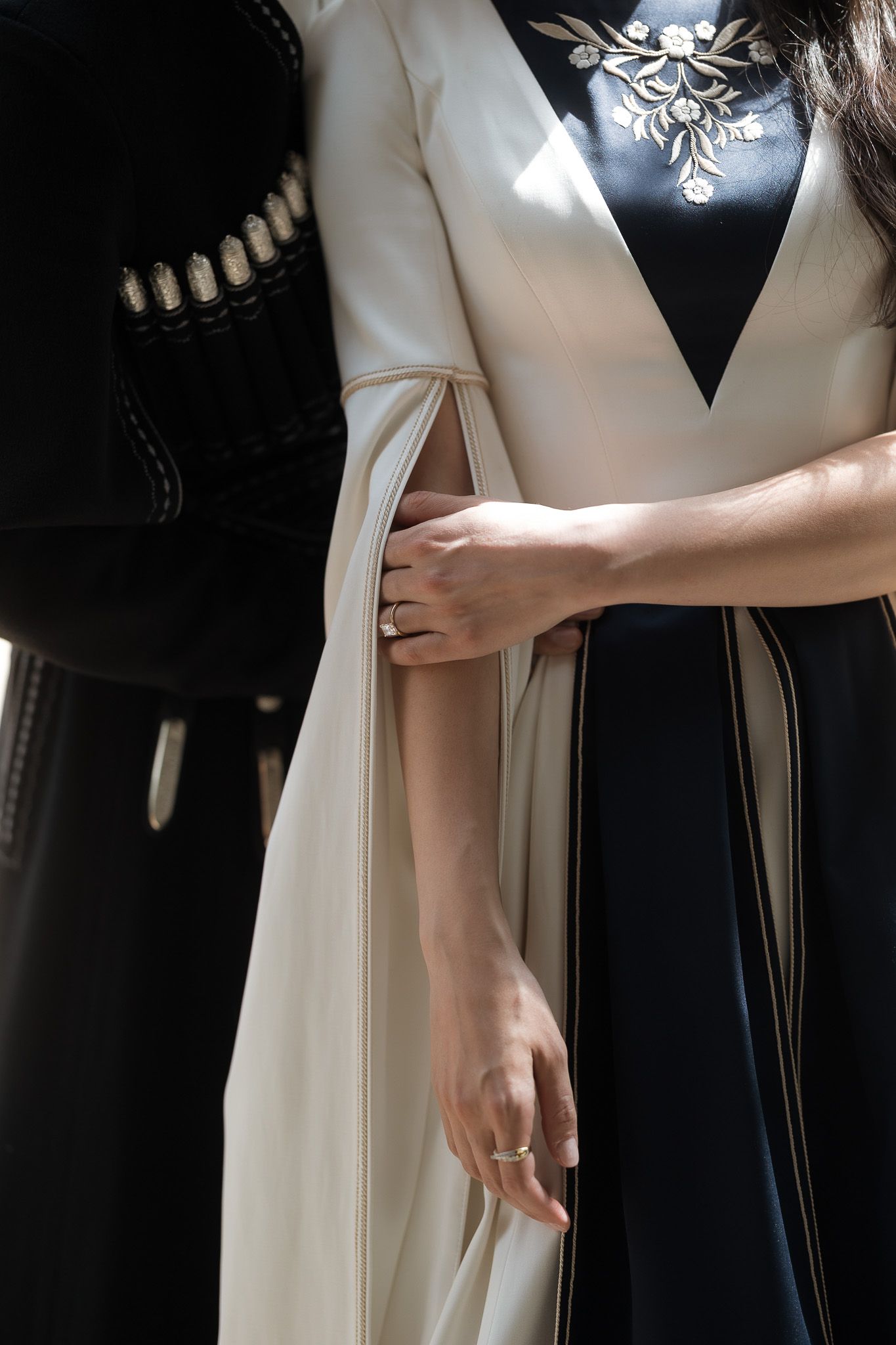 Two women in elegant black and white traditional embroidered gowns, one wearing rings, standing together.