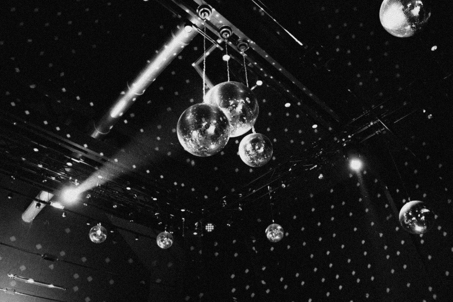 Black and white photo of disco mirror balls hanging from a ceiling with spotlights in a nightclub.