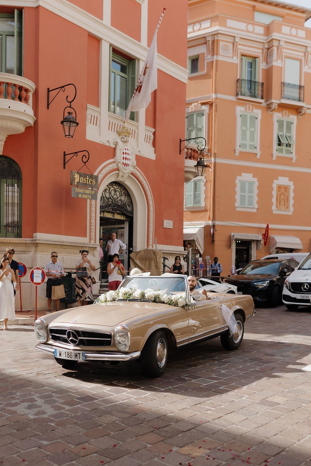 A row of vintage luxury Mercedes-Benz convertibles parked in front of a Mediterranean-style building with coral walls.