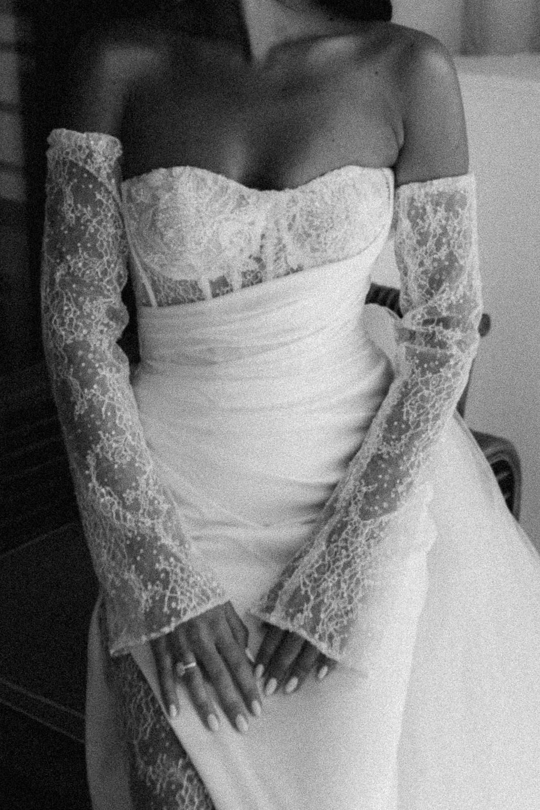 Close-up black and white photo of a strapless wedding gown with delicate lace sleeves and fitted bodice.