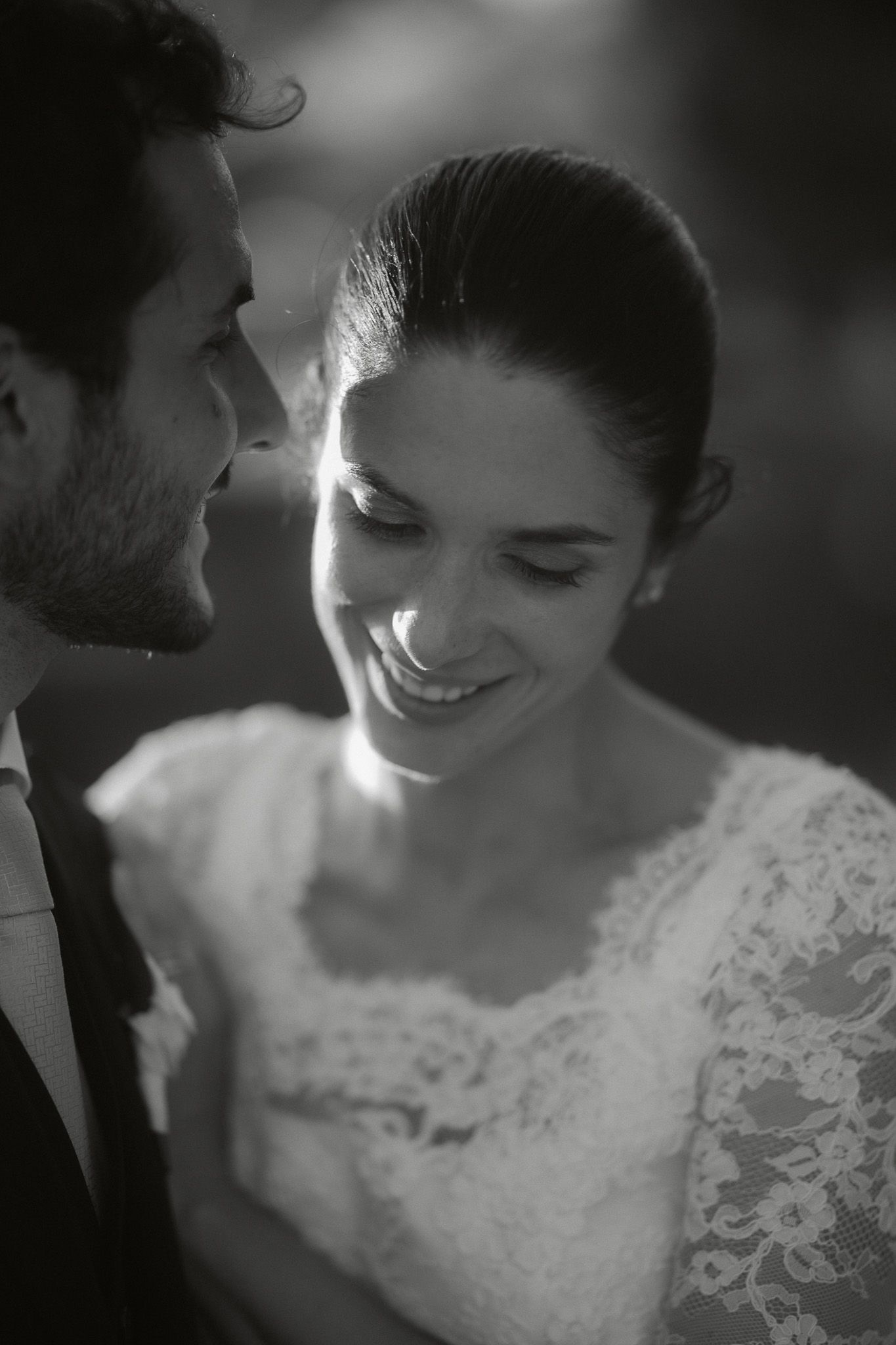 Black and white close-up of a smiling bride in lace dress sharing an intimate moment with her groom.