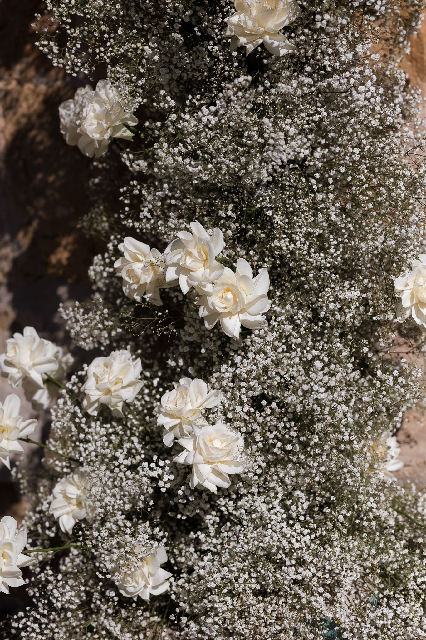 White roses and baby's breath flowers arranged against a dark rocky background.