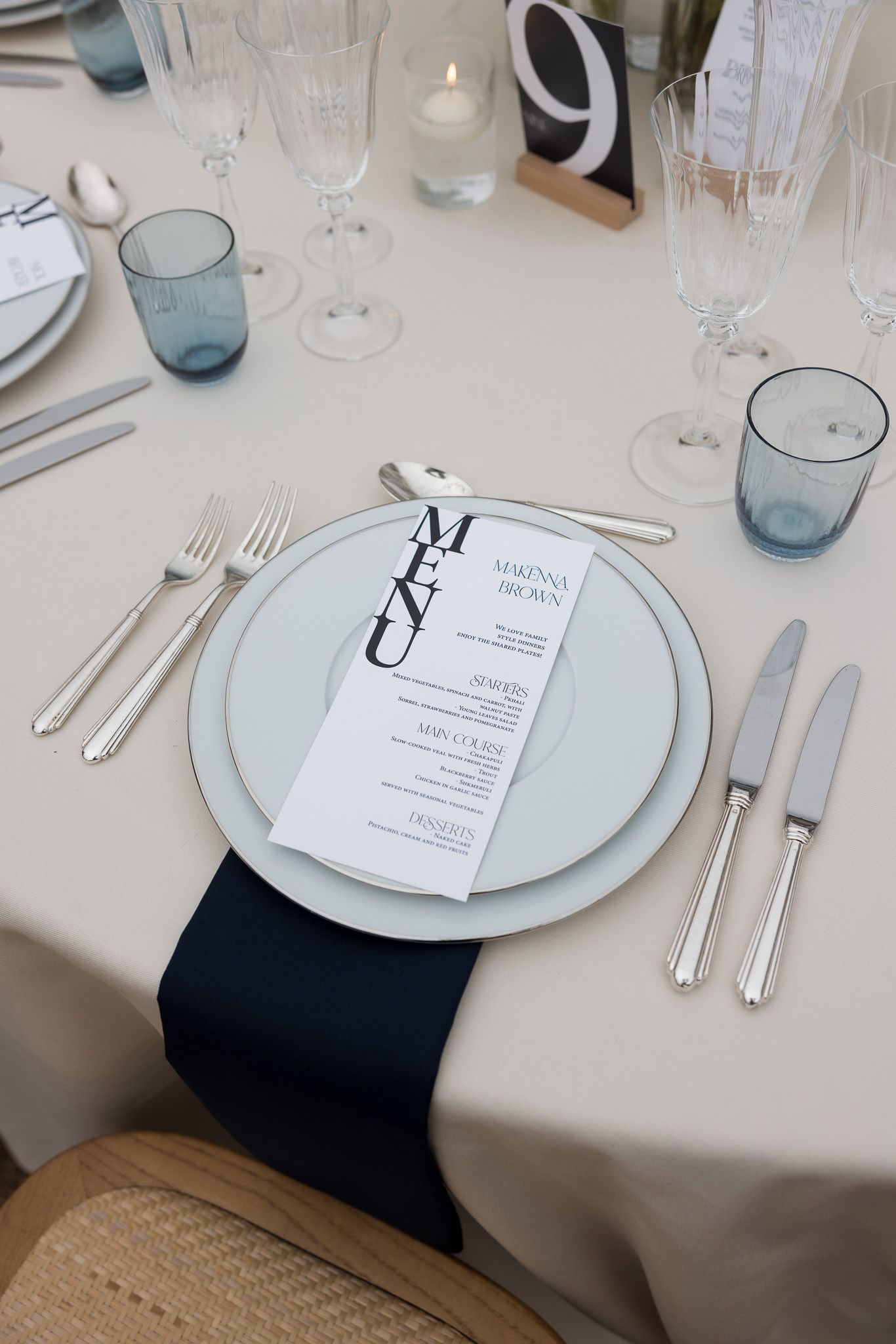 Elegant wedding table setting with navy blue accents, crystal glassware, silver cutlery, and a personalized menu card on white plates.