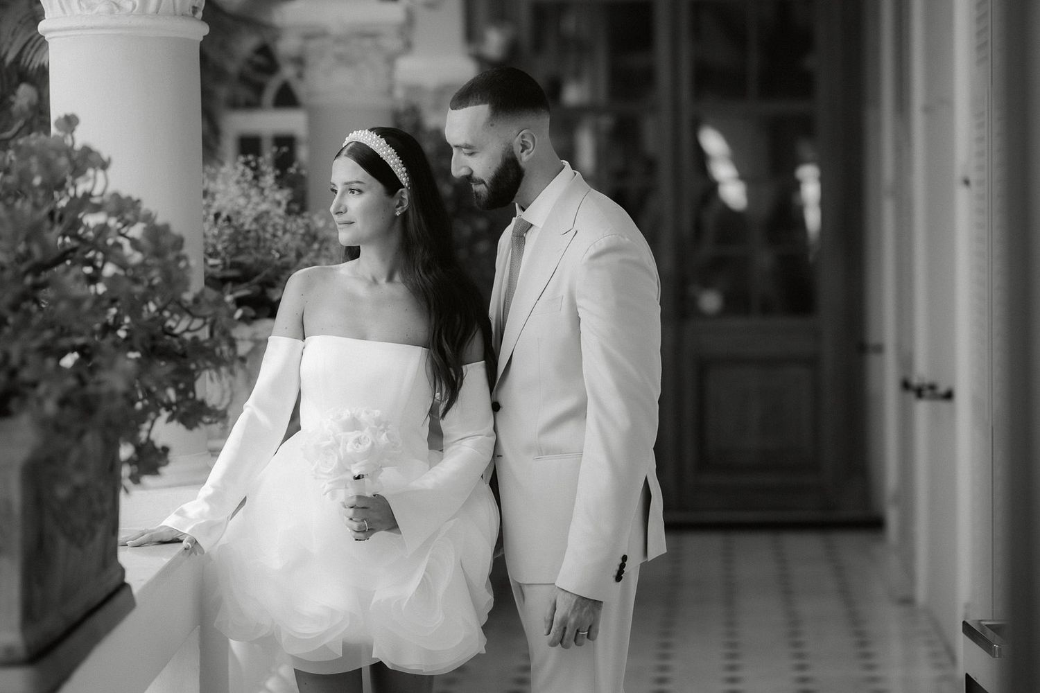 A wedding couple embraces and kisses in a romantic black and white moment captured in an outdoor setting.