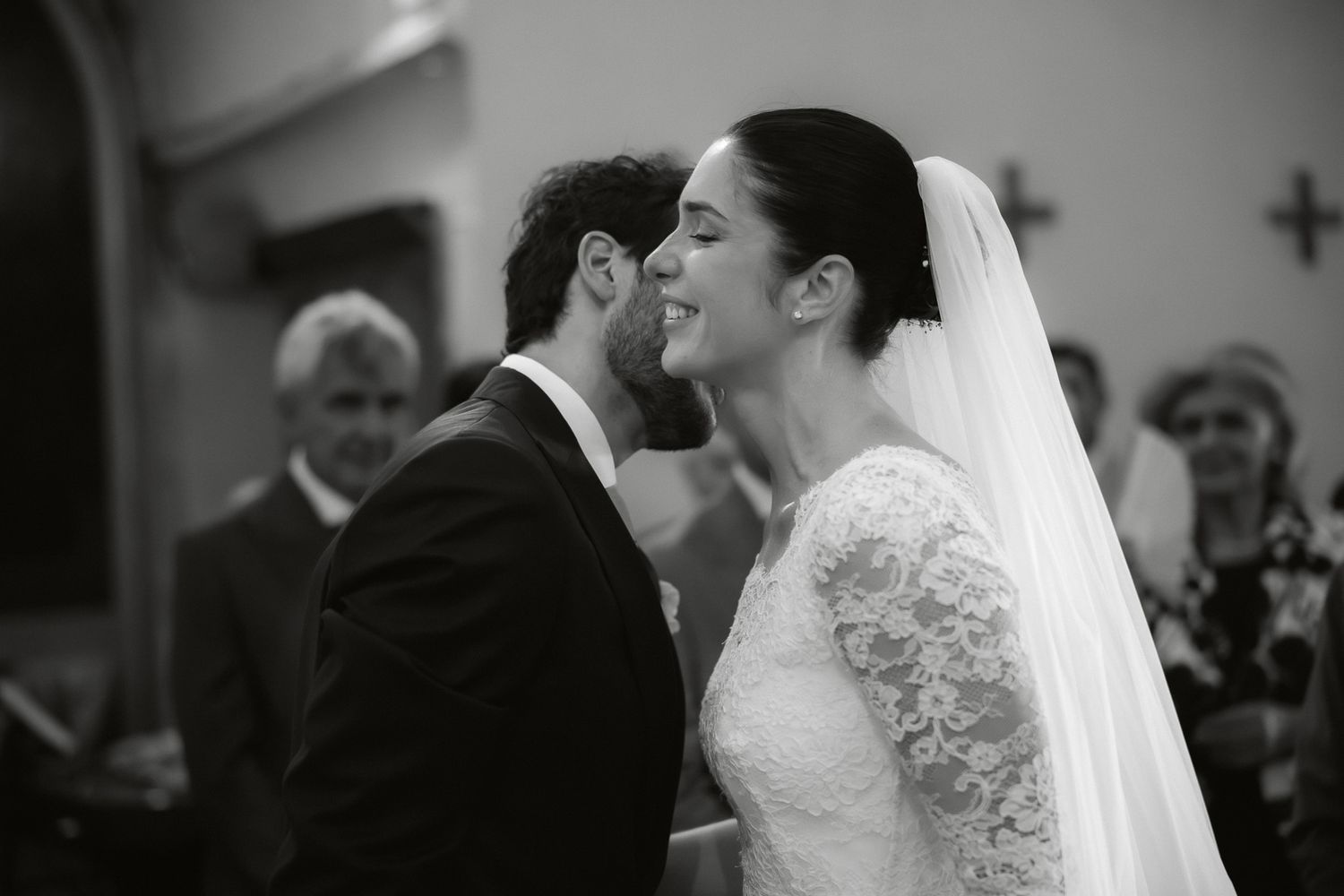 Black and white photo of a bride and groom sharing their first kiss at the altar during a church wedding ceremony.