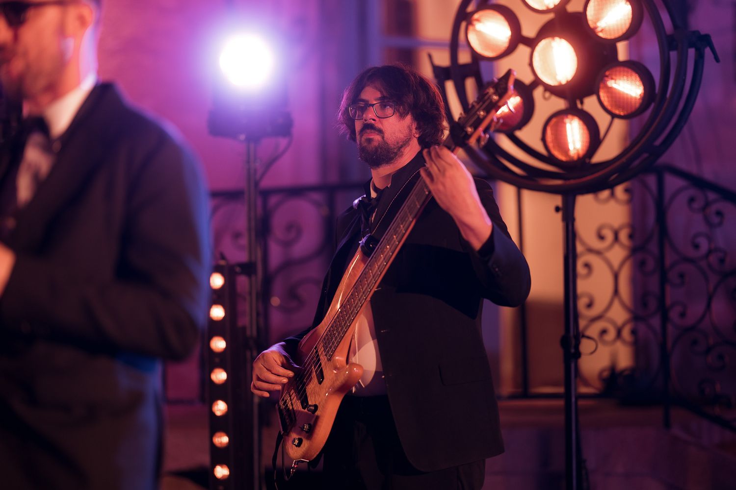 Musician playing electric bass guitar on stage with dramatic stage lighting at an indoor venue.