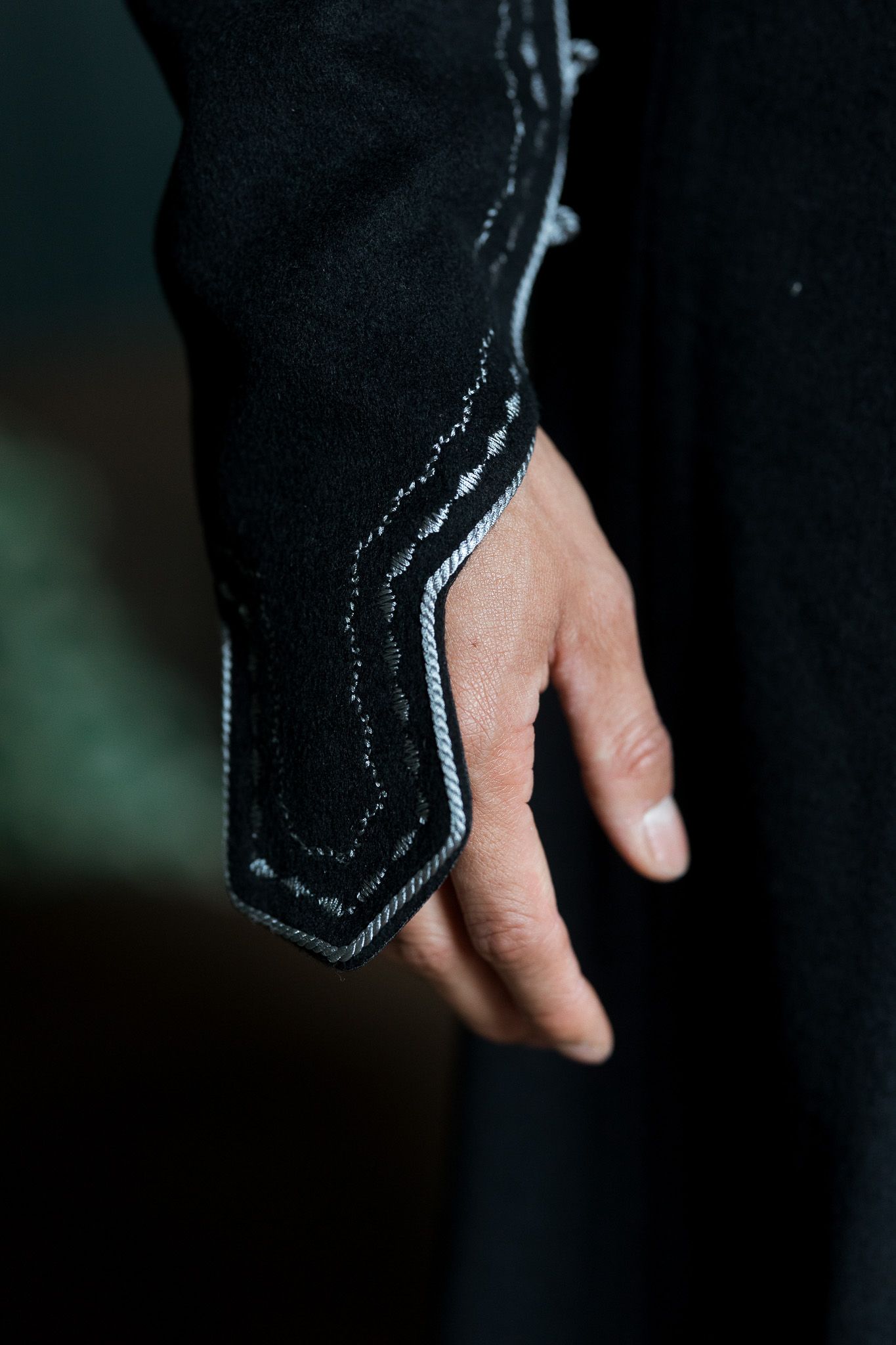 Close-up of a hand wearing a black embroidered sleeve cuff with intricate silver stitching detail.