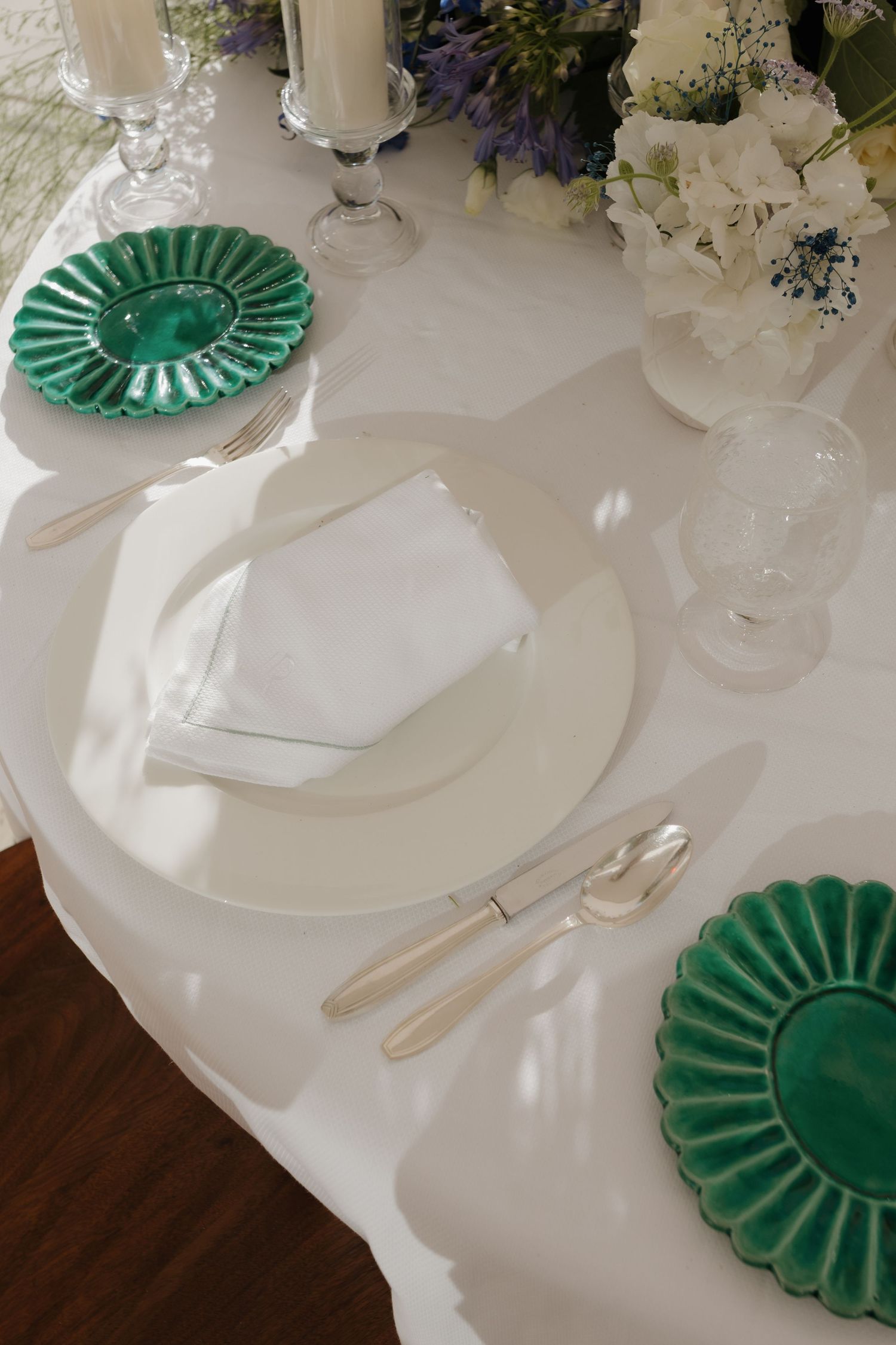 Elegant dining table setting with white linens, white plates, and emerald green scalloped charger plates.
