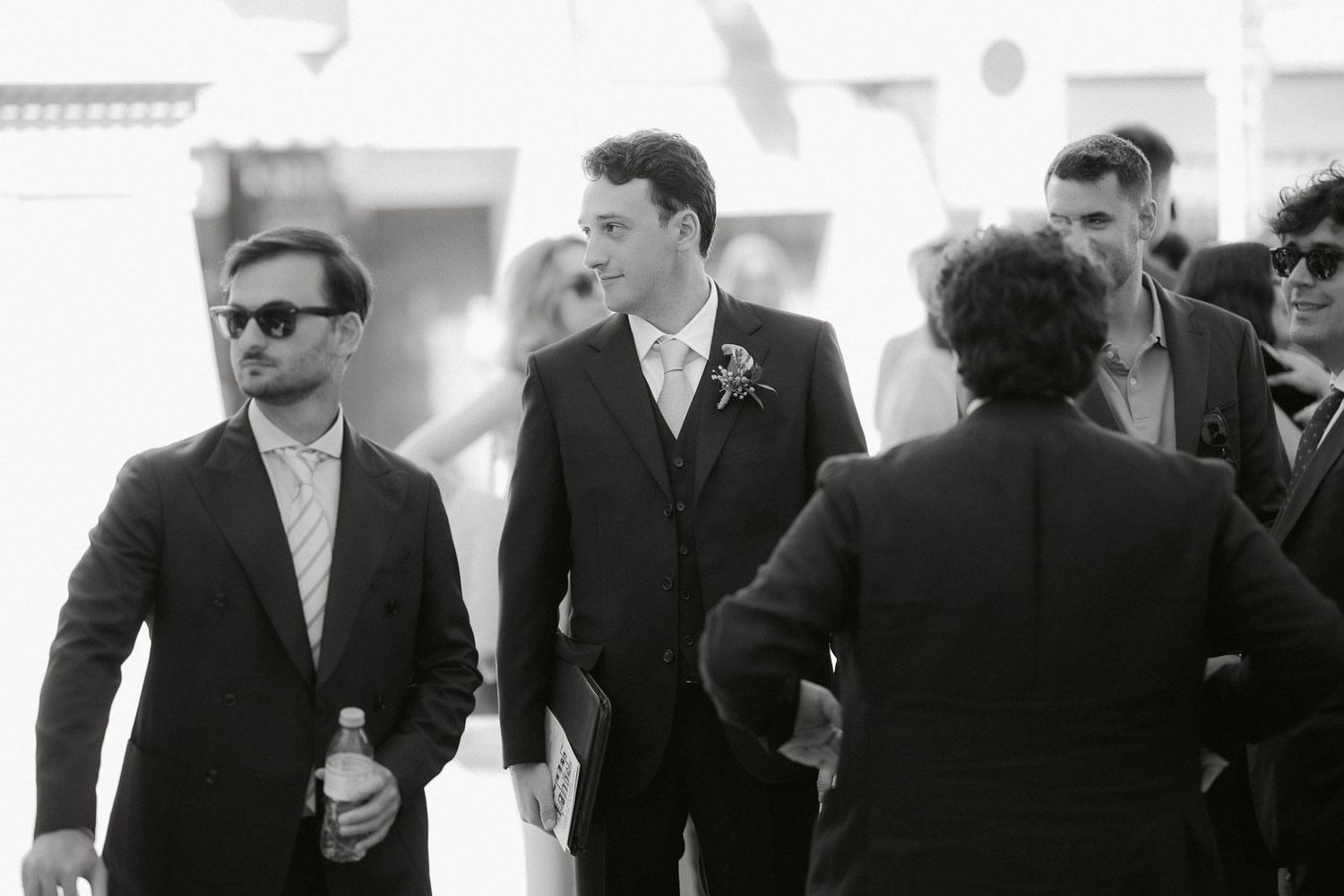 A black and white photo montage showing multiple angles of men in suits and sunglasses walking together.