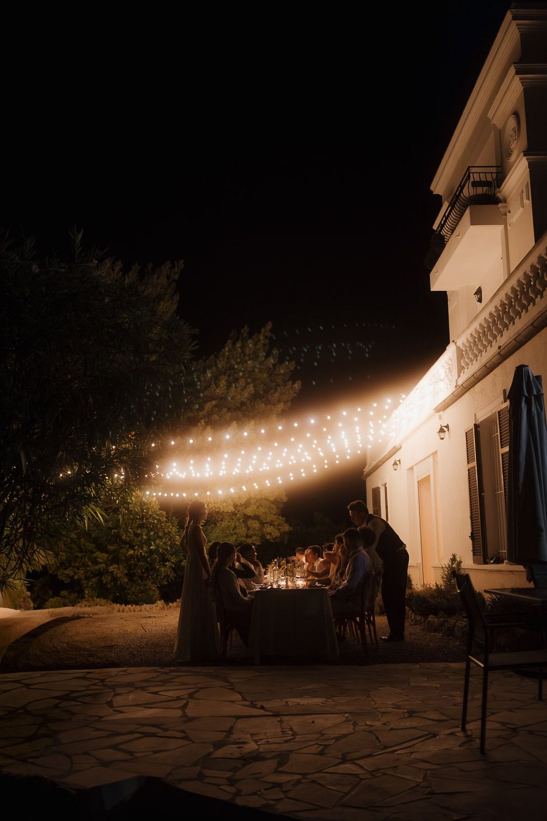 String lights illuminate a stone patio and house exterior at night creating a warm, inviting ambiance.