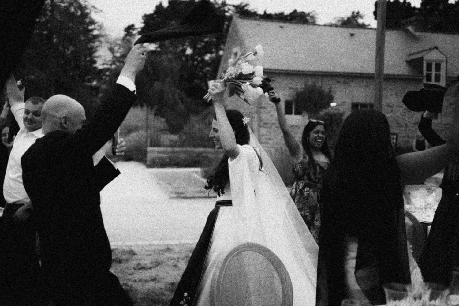 Black and white photo of a joyful bride and groom celebrating after their wedding ceremony outdoors.