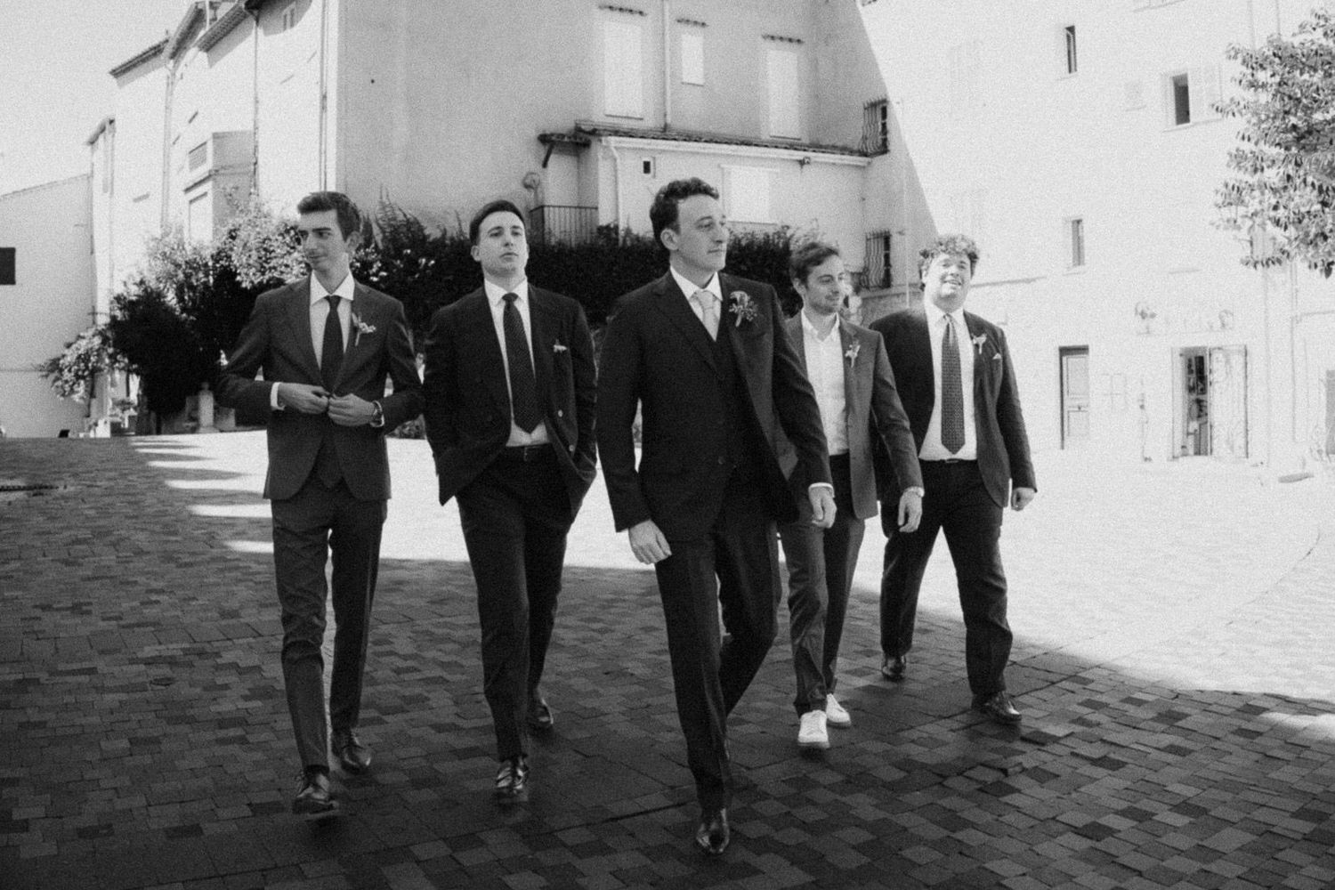 A vintage black and white photo of groomsmen walking down a cobblestone street in formal attire.