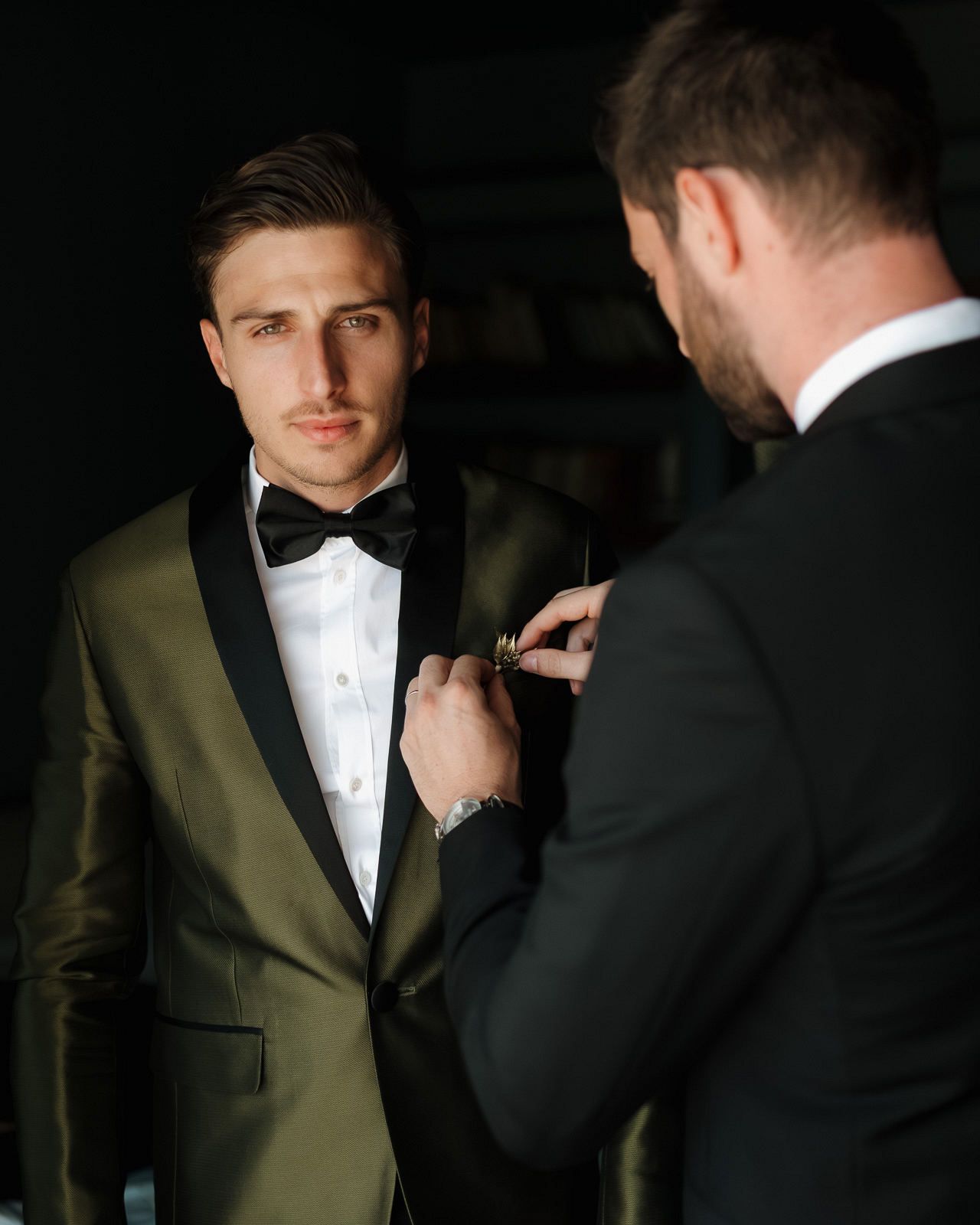 A sequence showing a man adjusting his bowtie while wearing a green suit and white dress shirt in dramatic lighting.