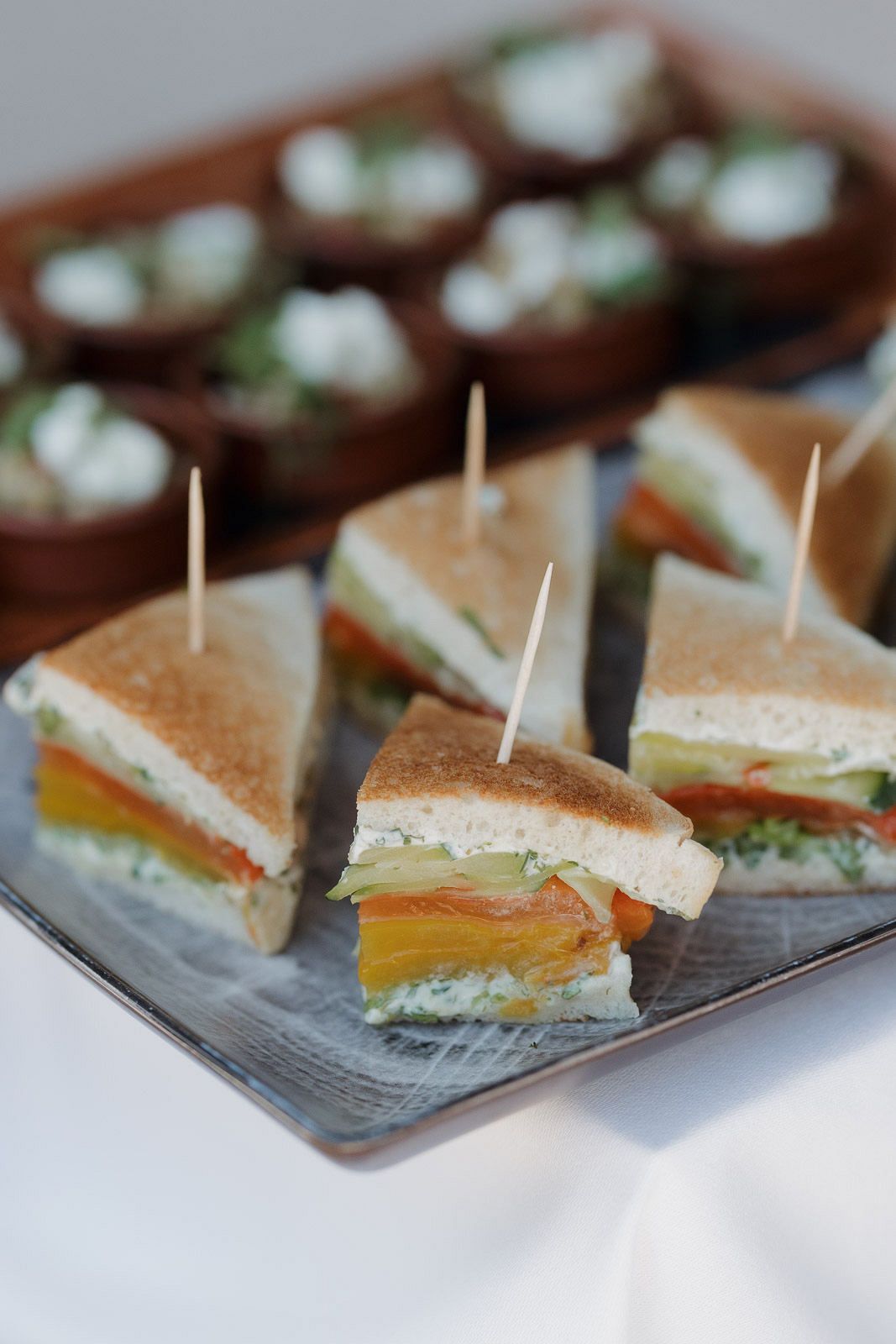 Mini triangle sandwiches with colorful fillings arranged on gray plates for a catered event.