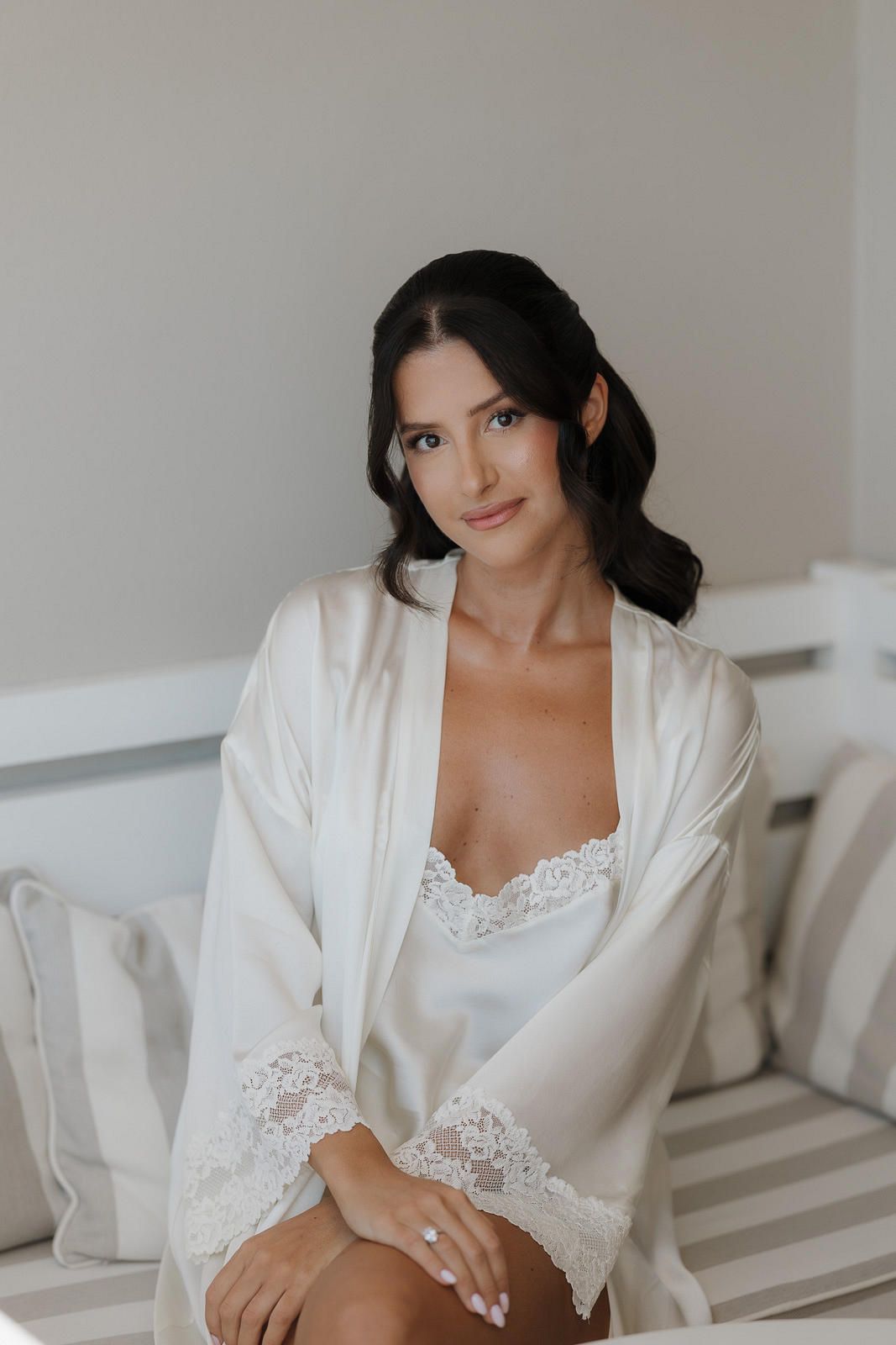 Woman in white lace lingerie and silk robe poses on bed during intimate boudoir photoshoot.