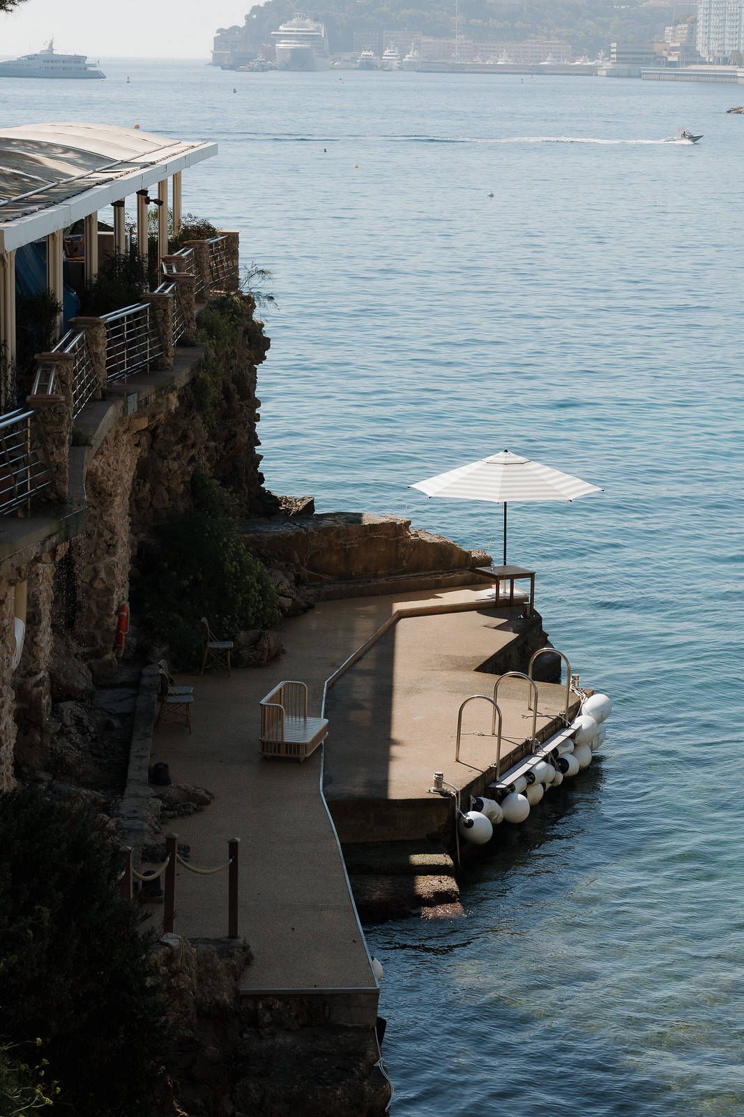 Wooden deck platforms extend over blue Mediterranean waters along a rocky coastline.