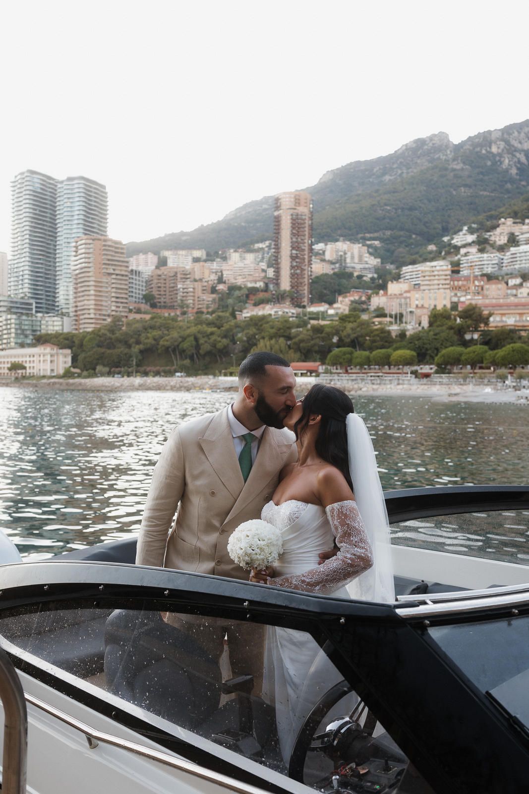 A romantic wedding couple shares intimate moments on a luxury yacht with Monaco's coastal cityscape in the background.