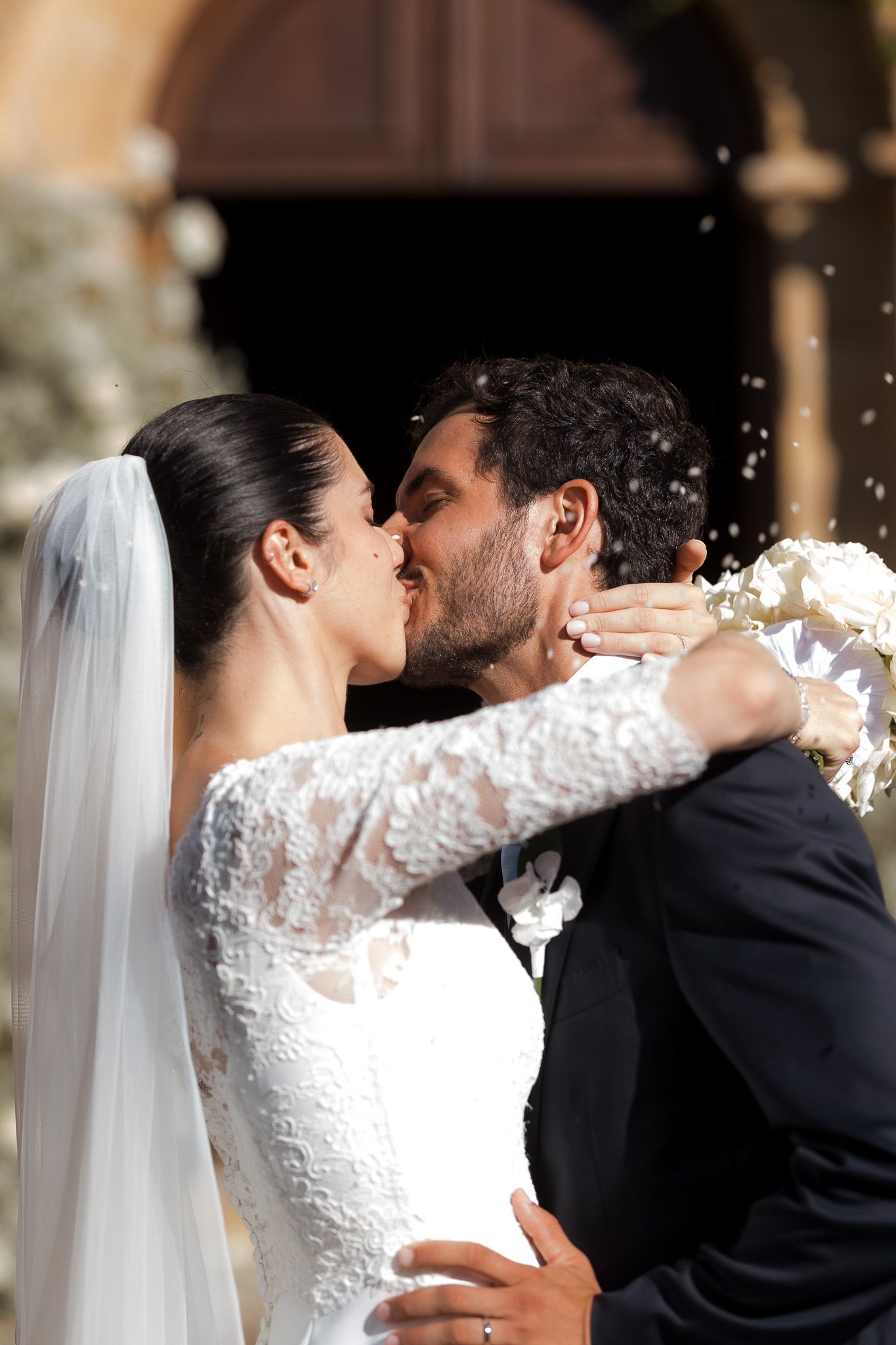 A bride and groom share a romantic first kiss outside a church, with rice falling around them on their wedding day.