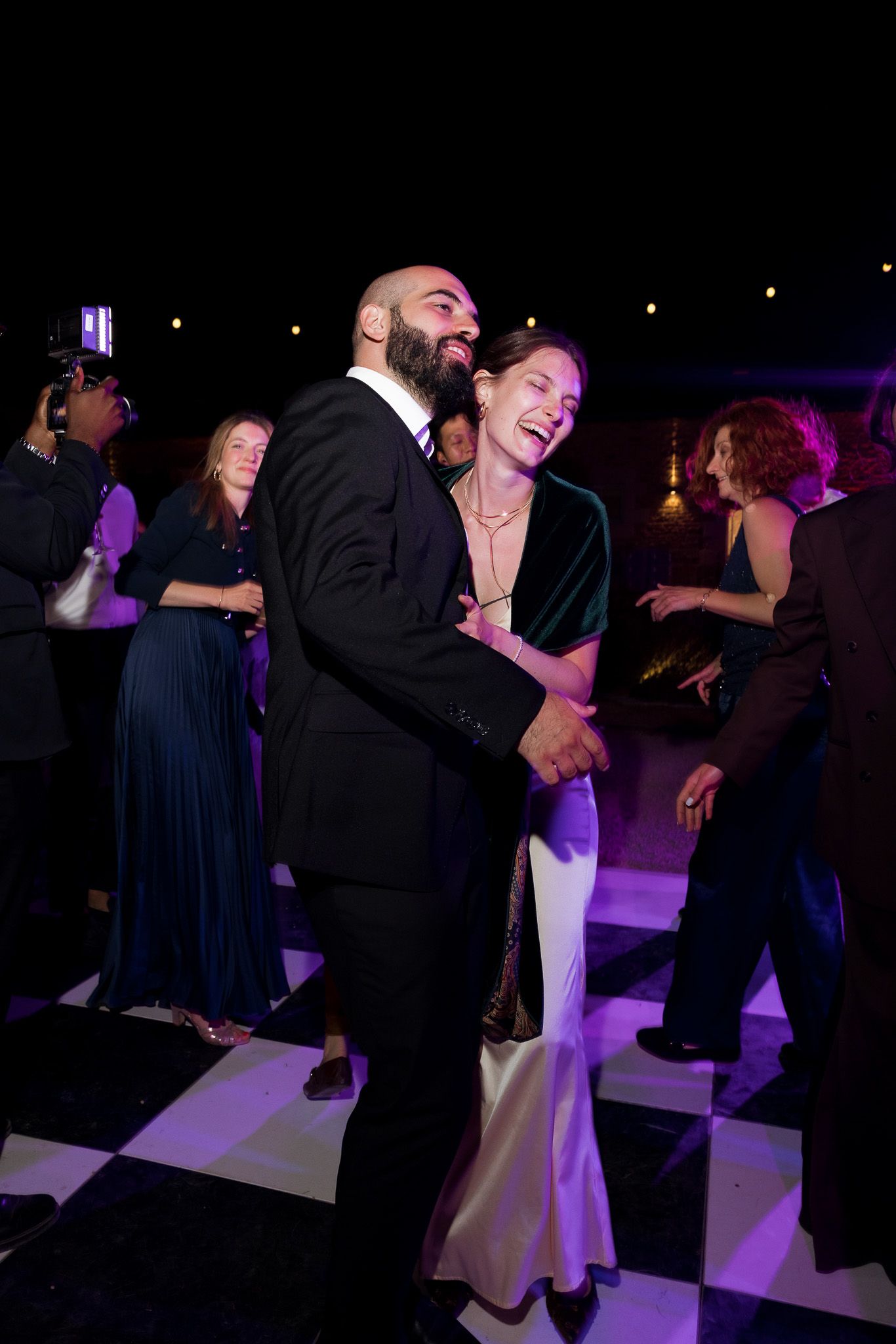 A couple laughs and dances together on a checkered dance floor at a formal evening event.