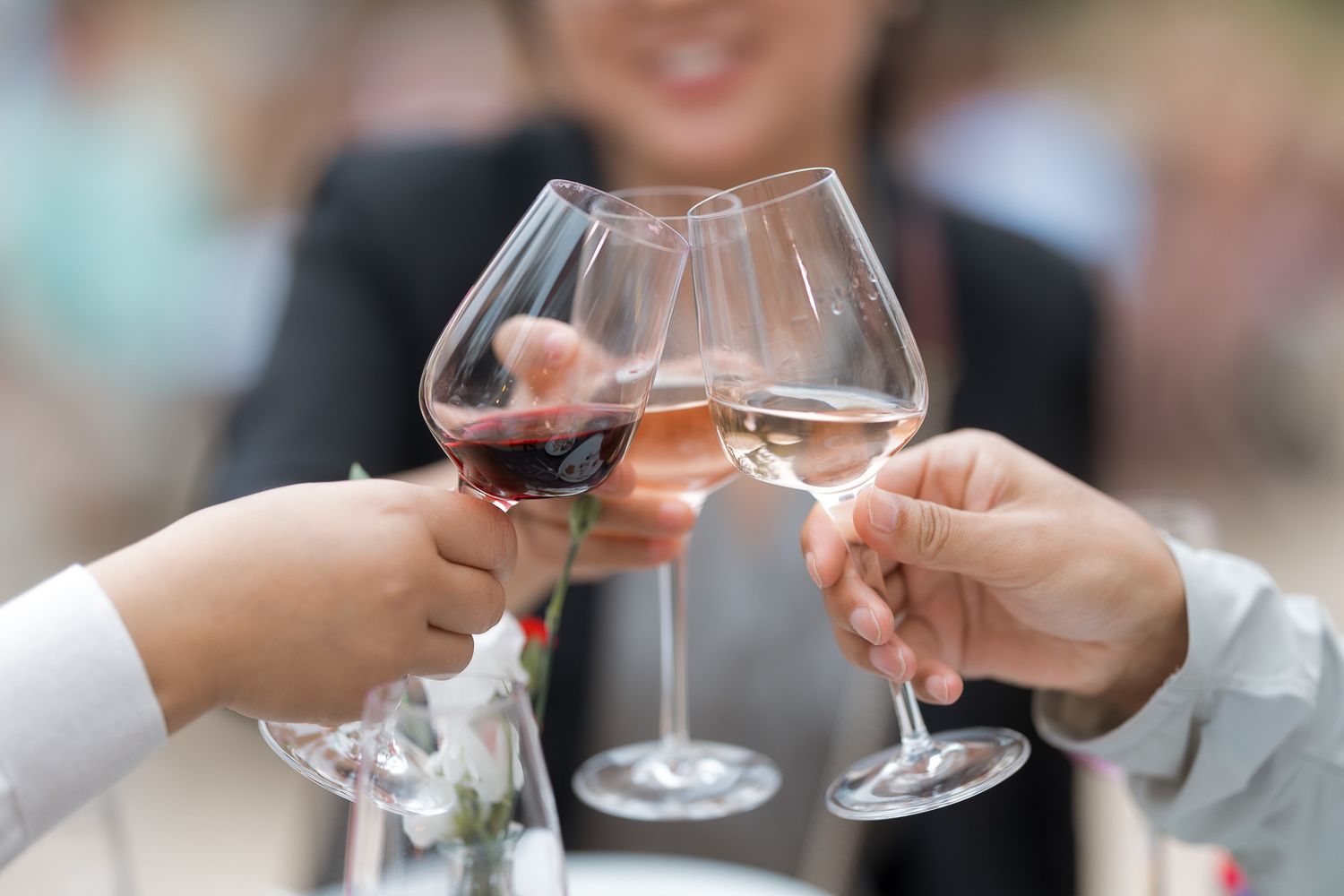 Three people toasting with red and white wine glasses at an outdoor celebration event.