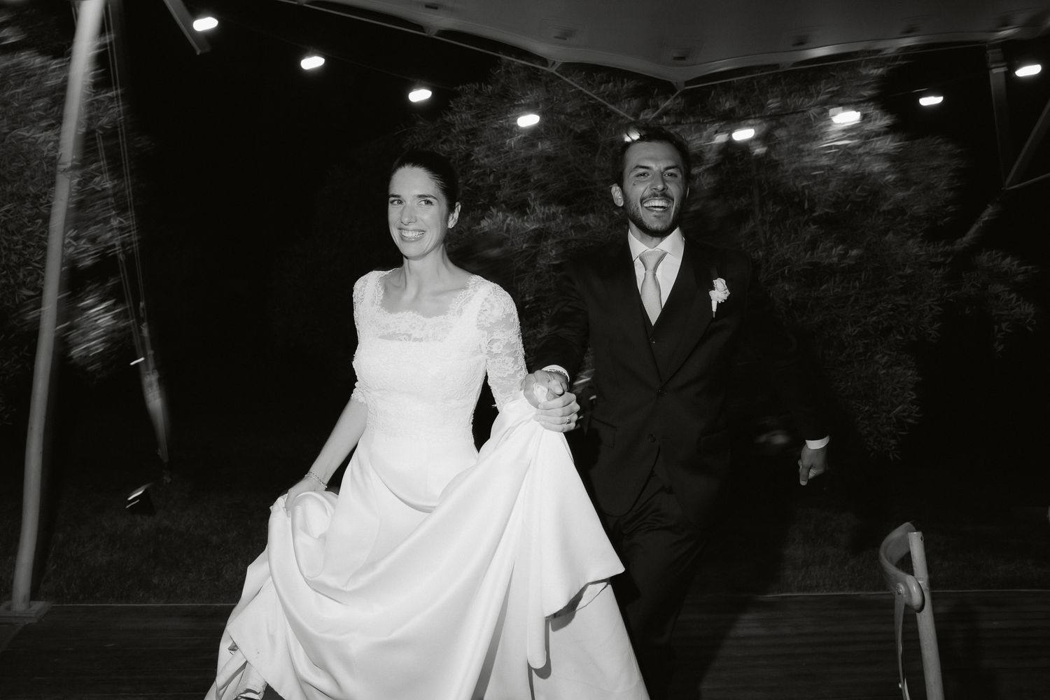 Black and white photo of a smiling bride and groom walking hand in hand at their wedding reception.
