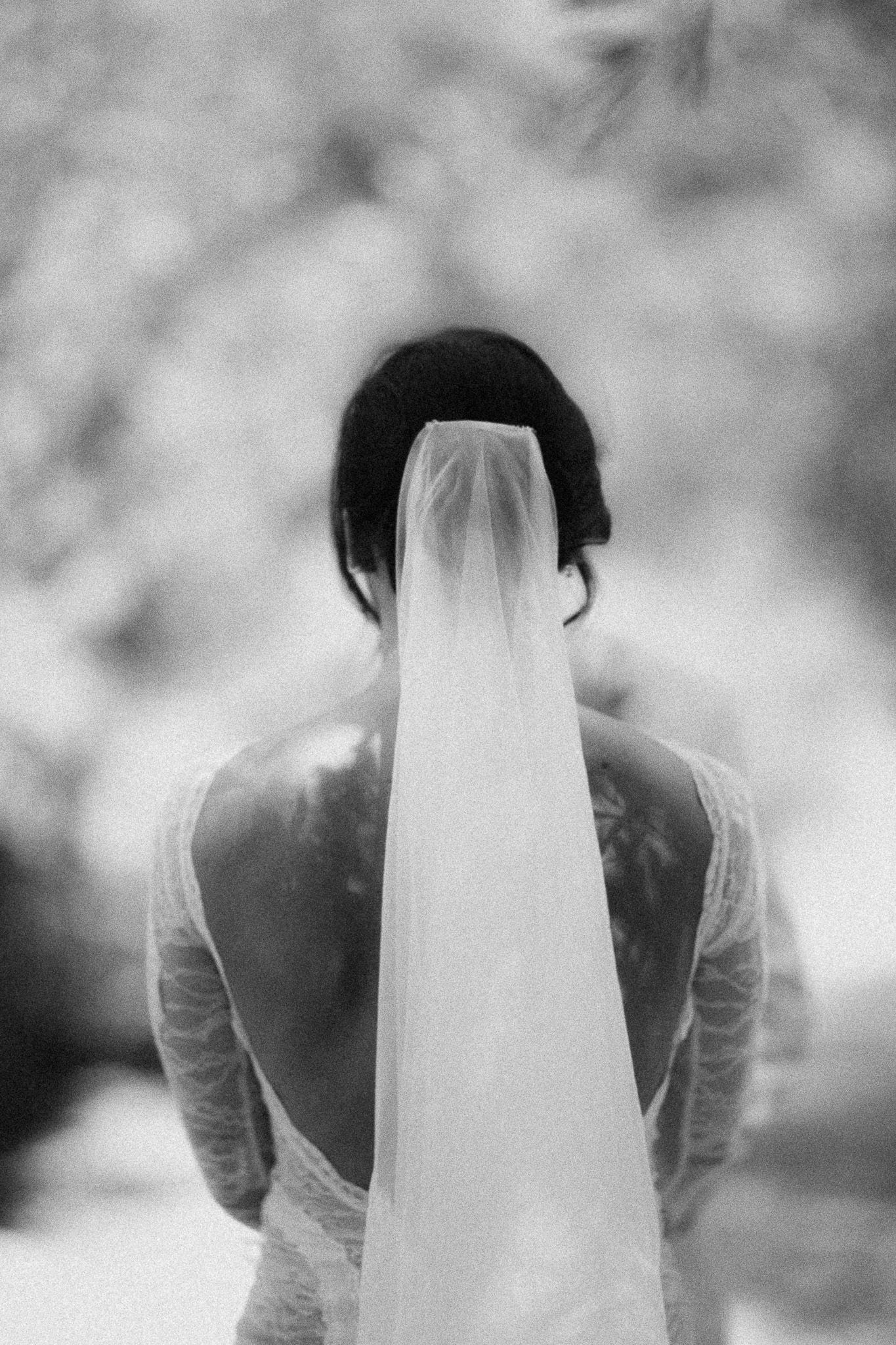 Black and white photo of a bride from behind, showcasing her elegant wedding veil and lace dress.