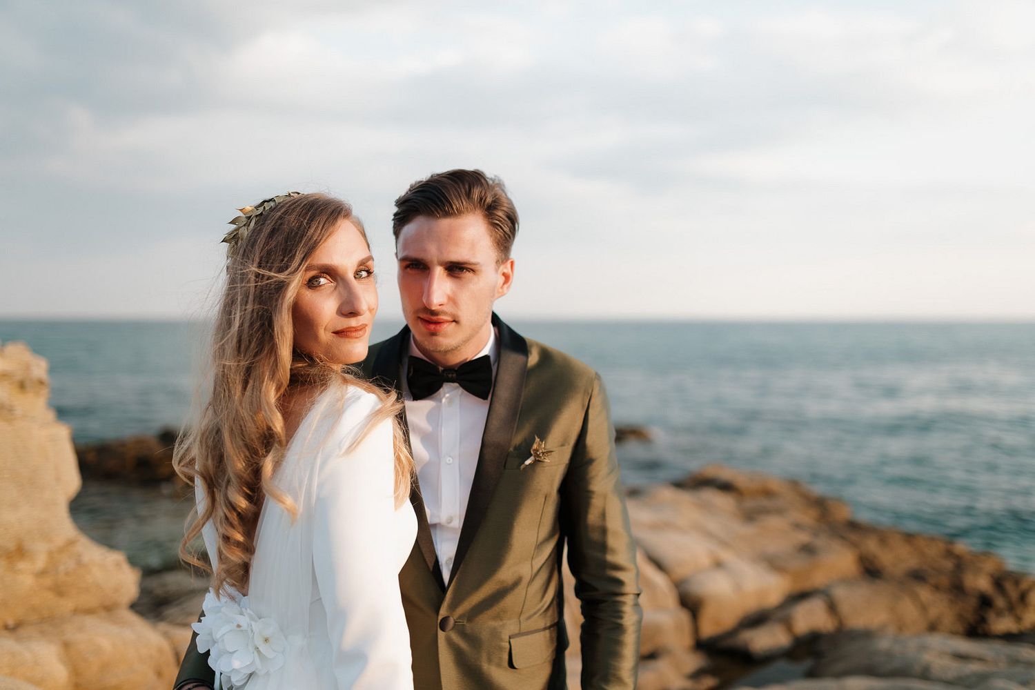 A couple shares an intimate moment on rocky coastal cliffs overlooking the ocean at sunset.
