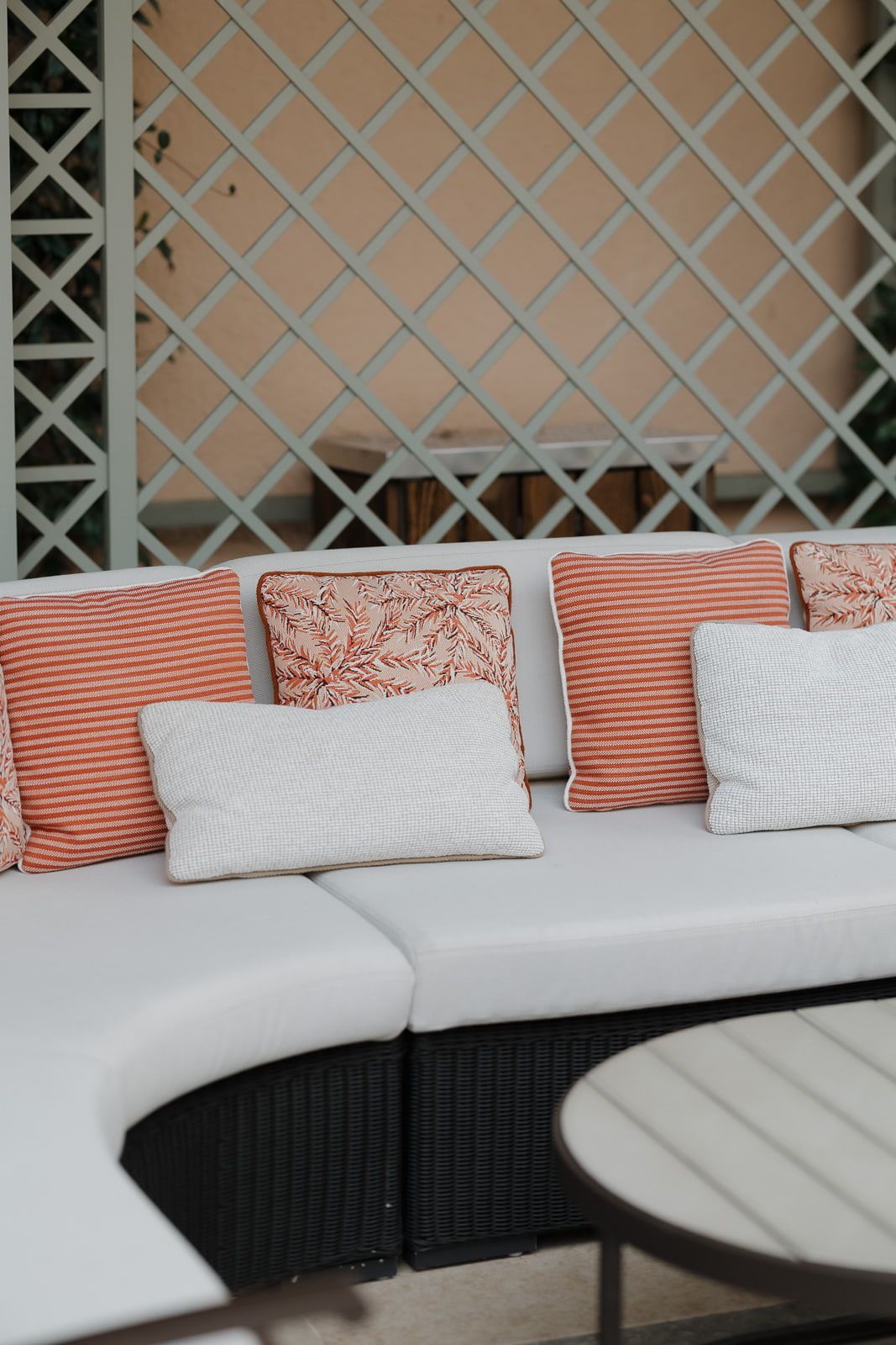 A curved outdoor lounge area with white cushions and coral striped pillows against a lattice wall backdrop.