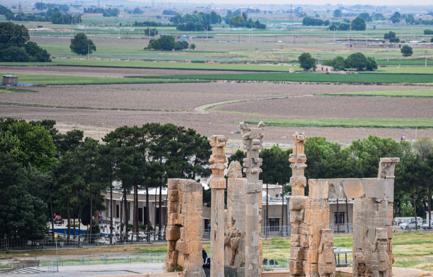 Aerial view of Persepolis ruins with surrounding agricultural landscapes and modern roads.