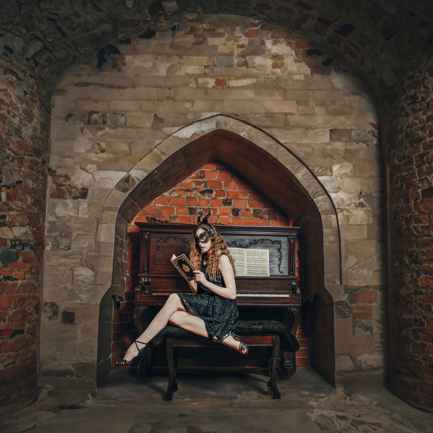 Artistic photo of person in masquerade outfit seated at piano in stone archway.
