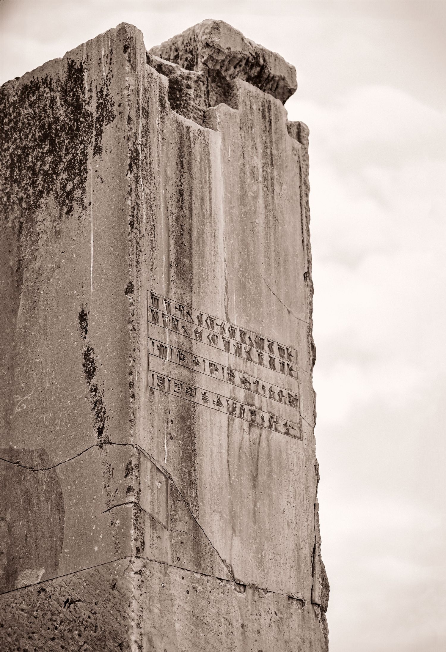 Ancient stone monument with weathered inscriptions carved into a tall vertical pillar against cloudy sky.