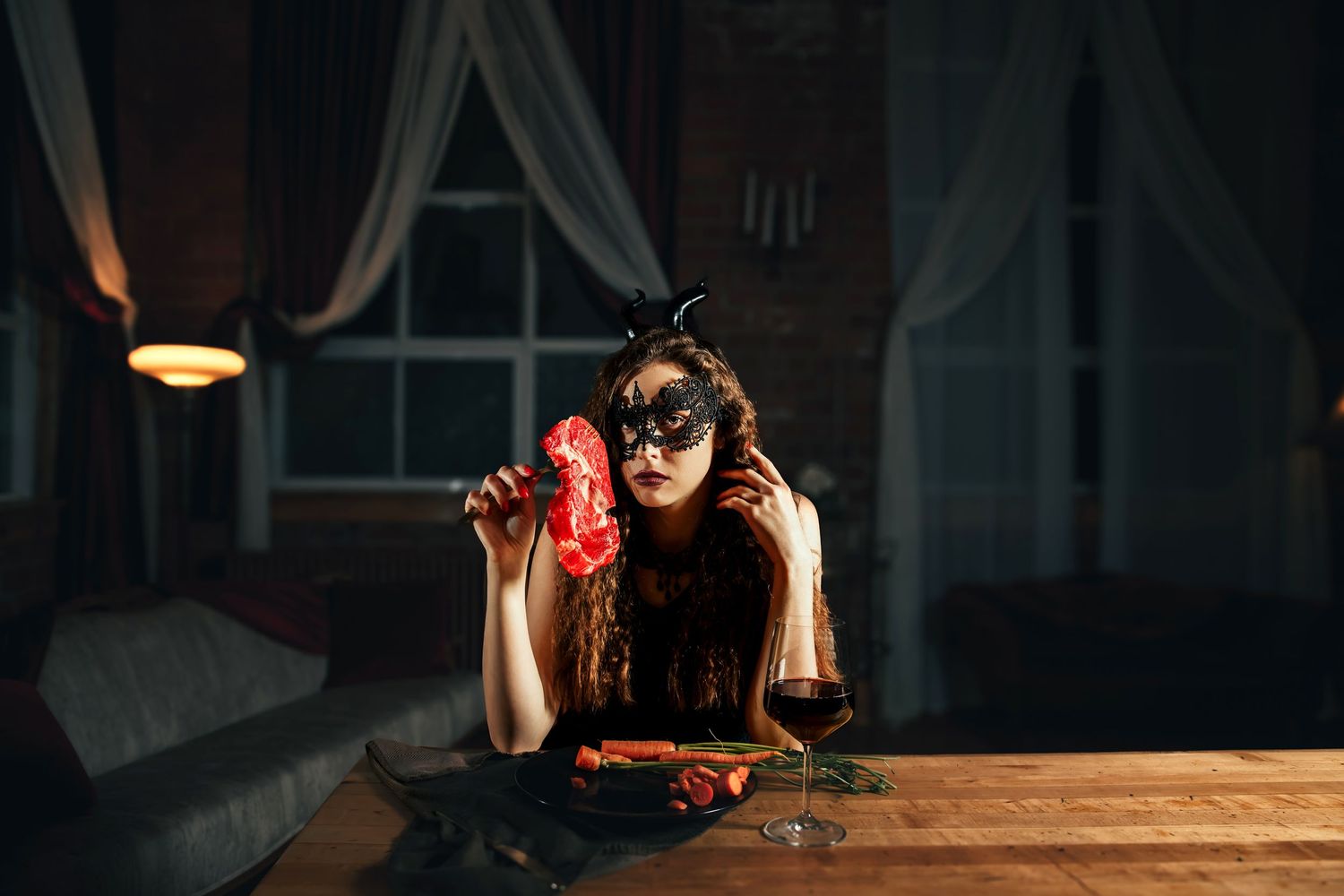 Moody nighttime scene with masked figure drinking red beverage at wooden table.