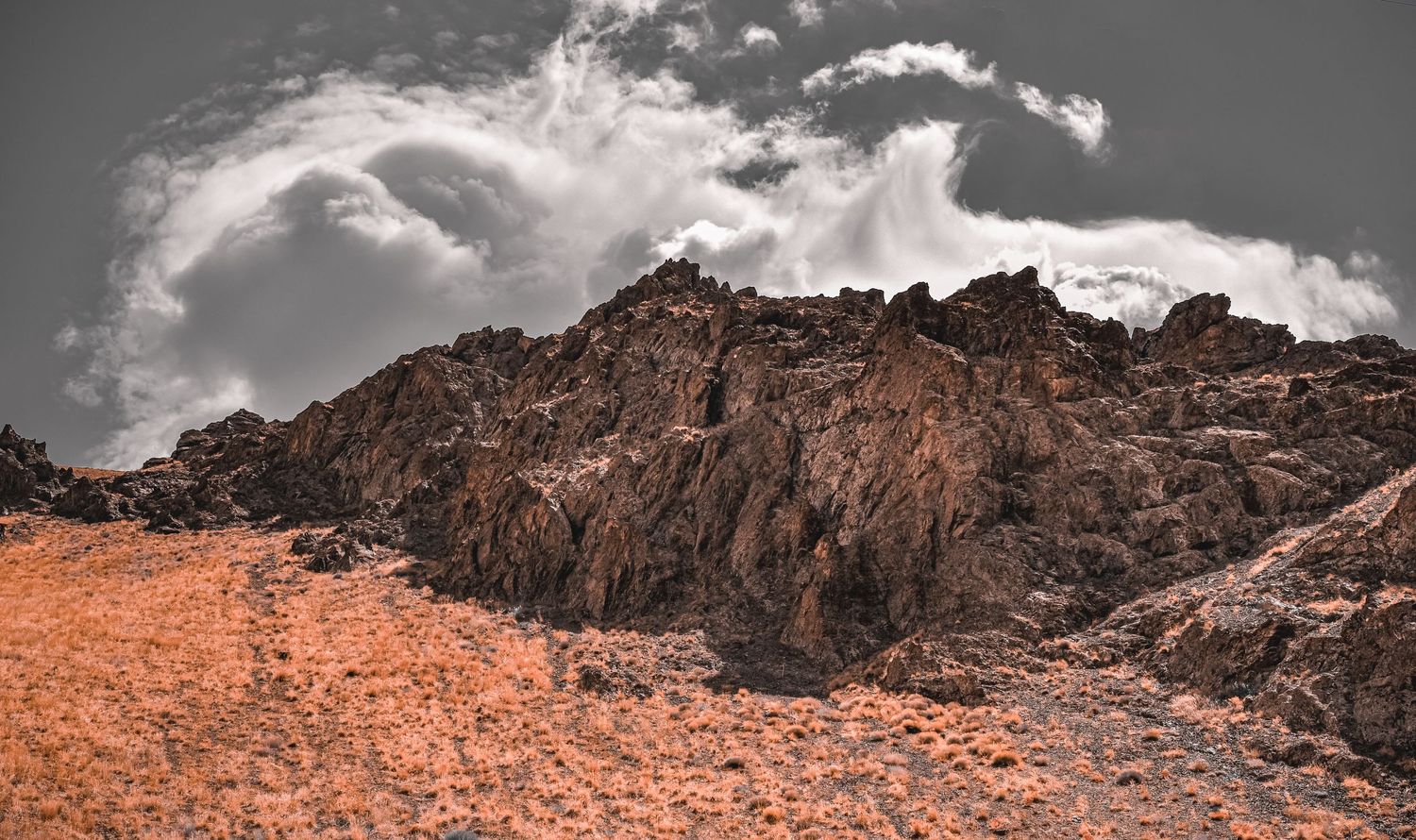 Rocky mountain peak under dramatic cloudy sky in sepia tones.