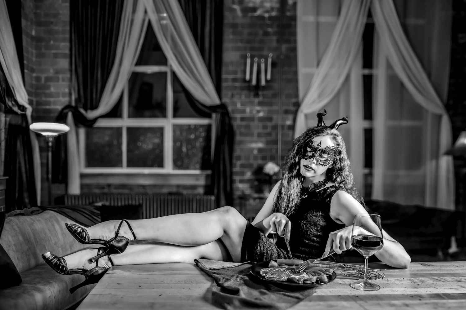 Black and white photo of lounging figure with mask at dining table with vintage decor.