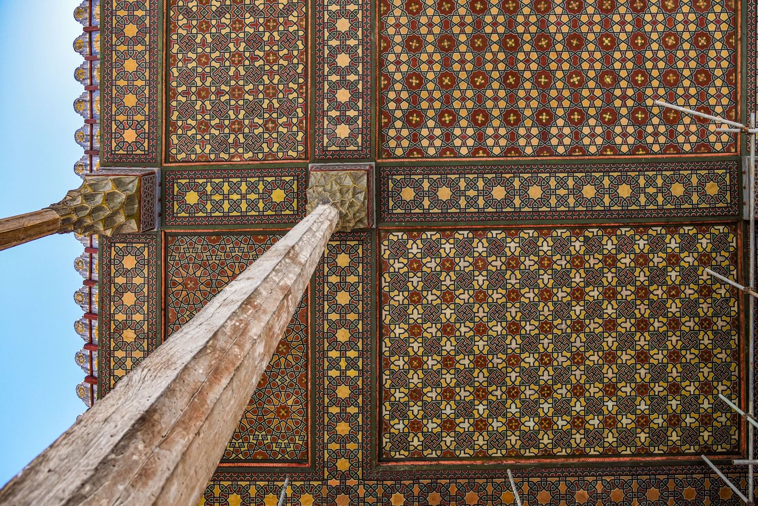 Detailed view of geometric Islamic patterns and ornate tilework on a mosque ceiling against blue sky.