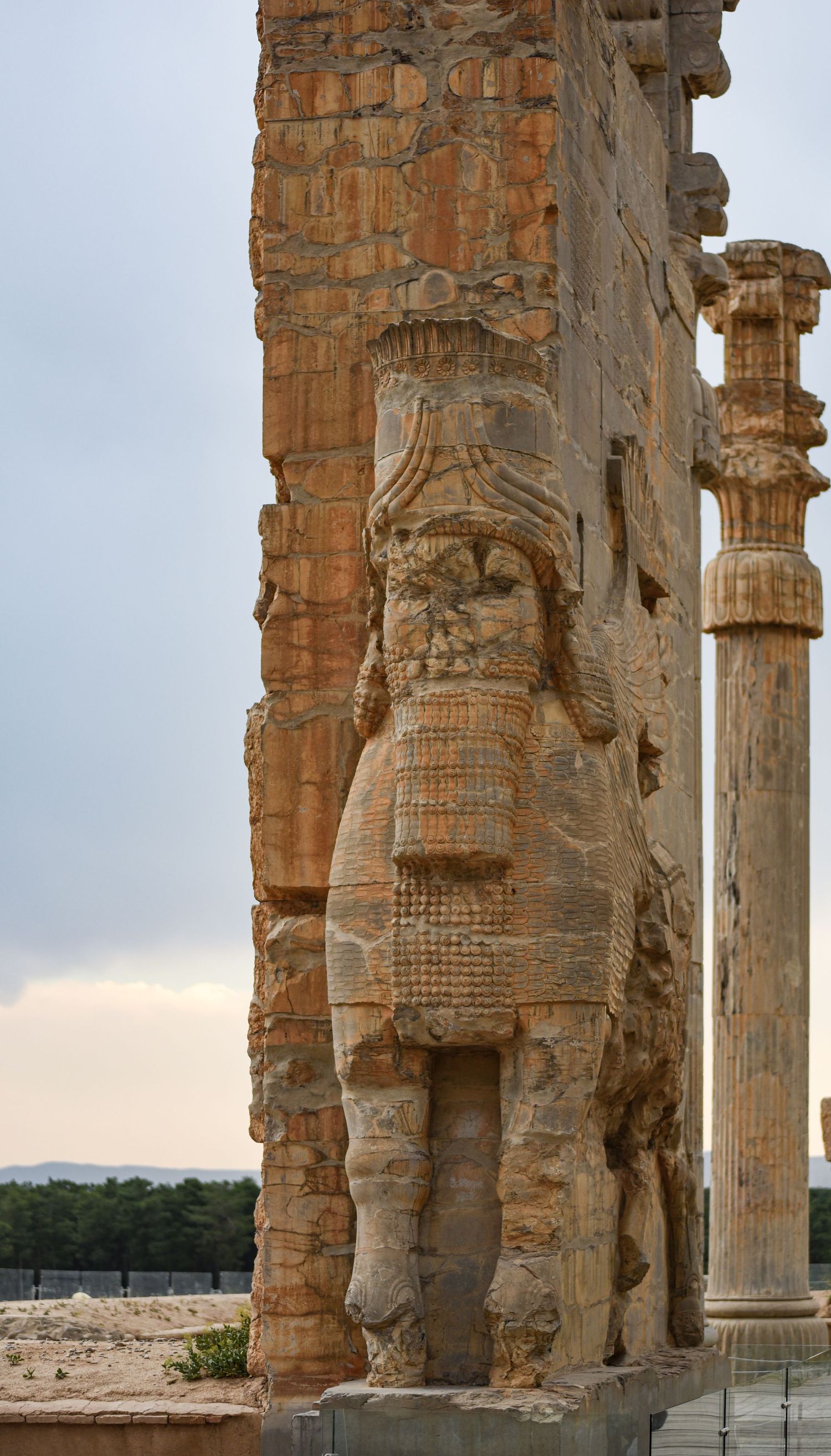 Ancient carved stone figure relief on weathered column at historic Persepolis site.