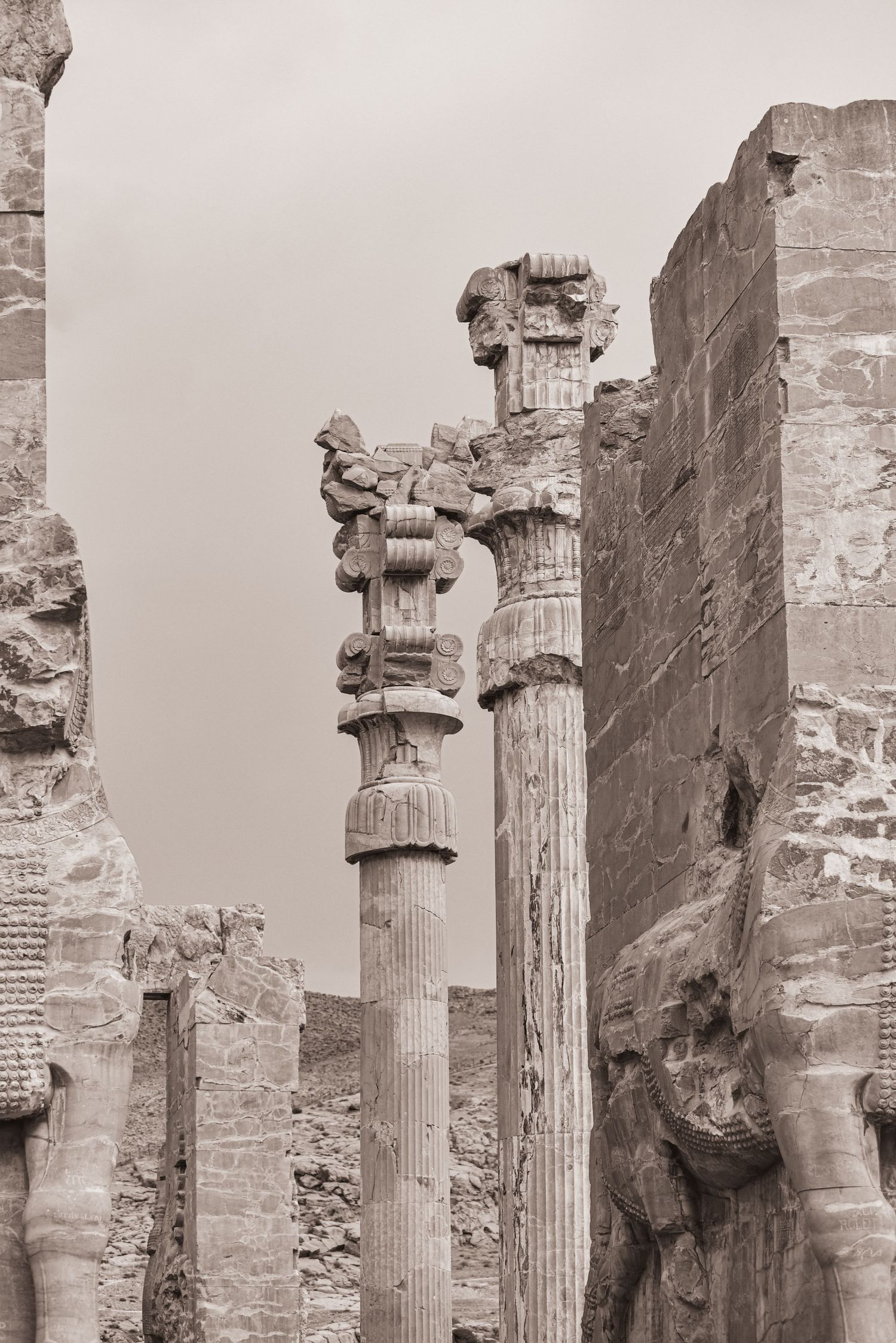 Ornate Corinthian columns stand amid ancient ruins in sepia tones.