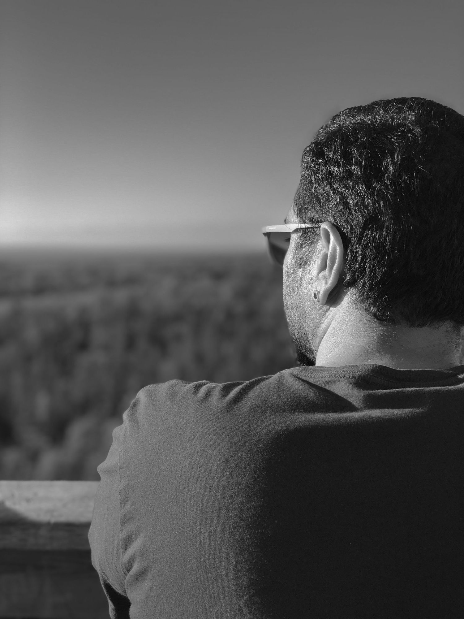 Black and white profile view of person wearing glasses looking out over landscape.