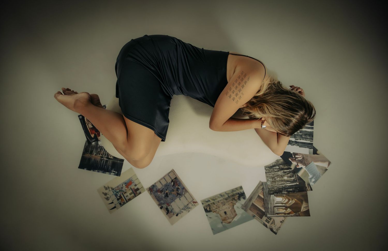 Person curled up on floor surrounded by scattered photographs in moody lighting.