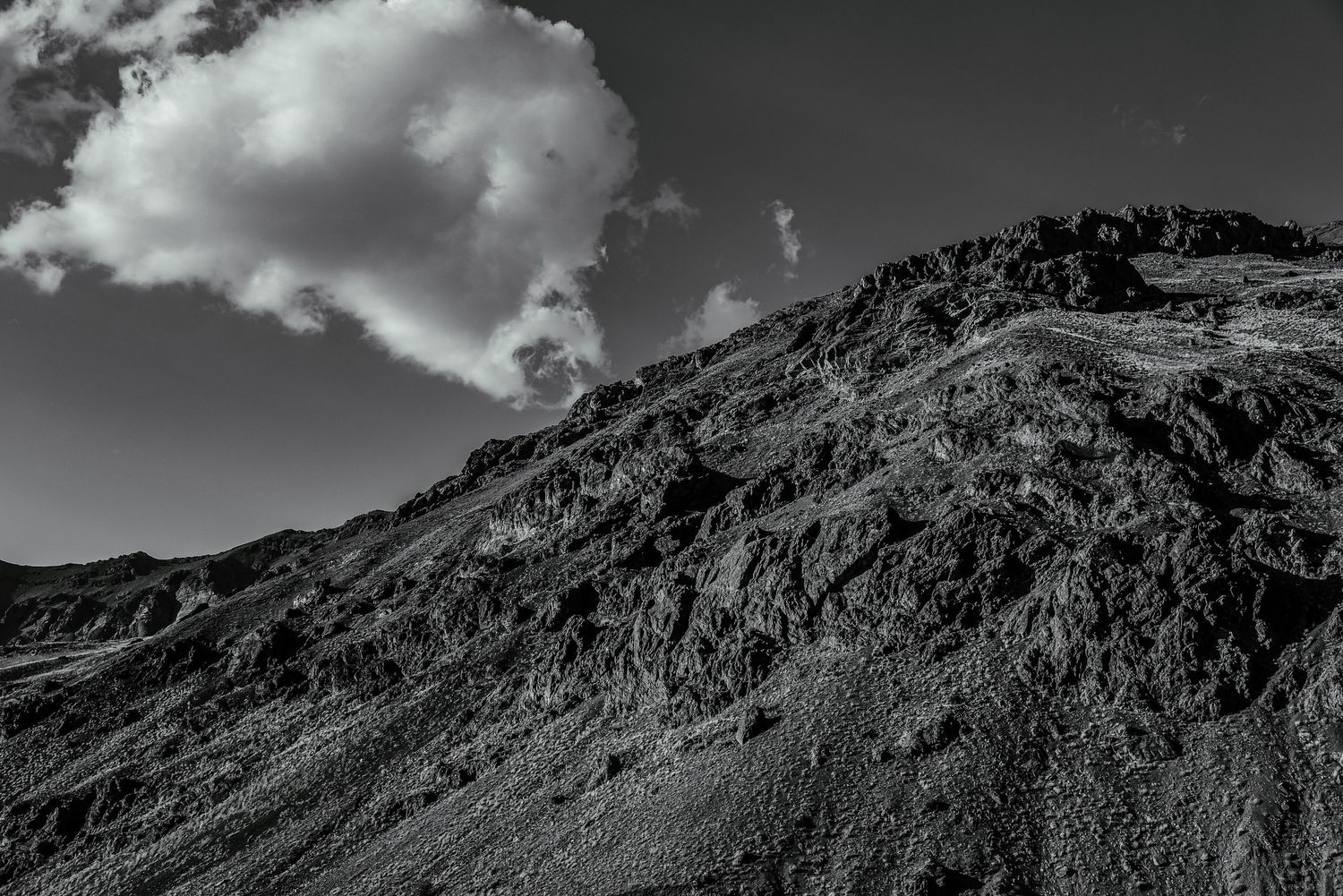 Stark black and white mountain peak with dramatic cloud formation in sky.